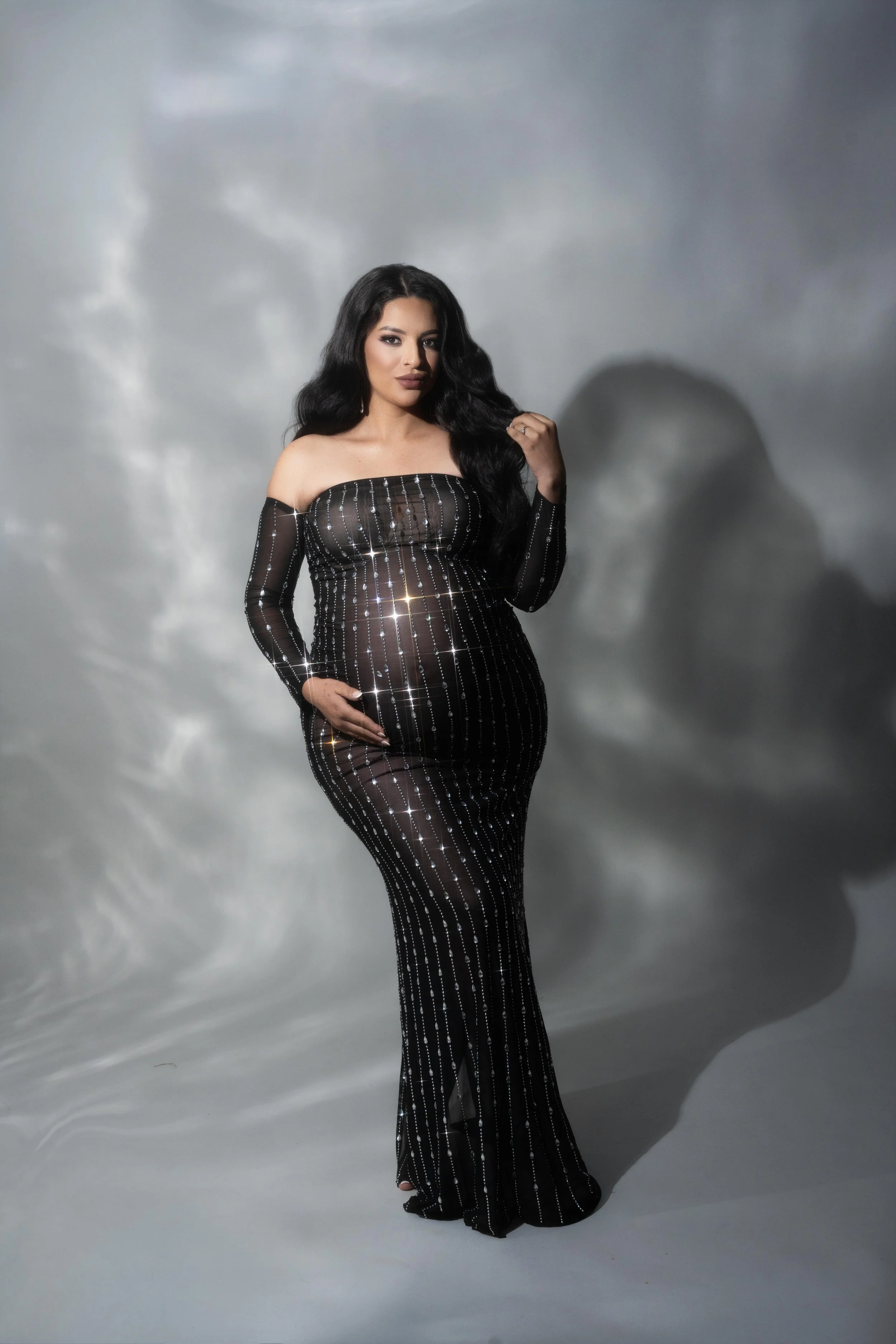 Elegant maternity portrait in a black beaded gown with dramatic studio lighting, photographed in Plano, Texas.