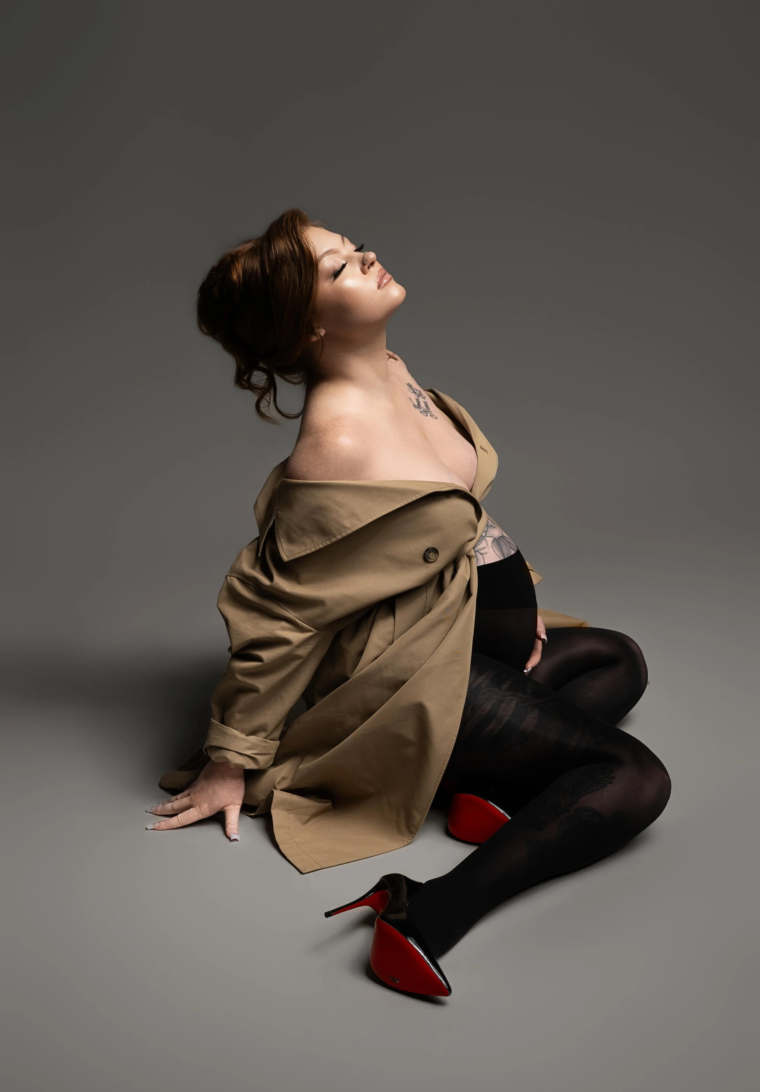 Editorial Dallas maternity portrait featuring a mother-to-be in a fashion-forward seated pose with dramatic studio styling.