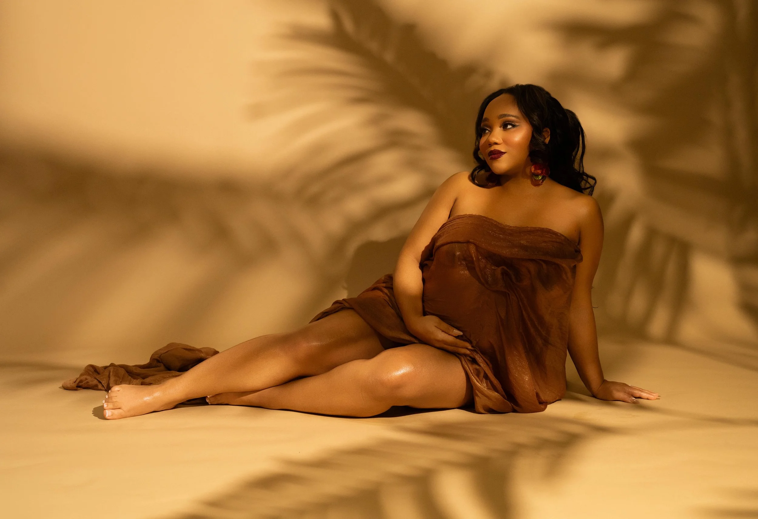 Pregnant woman in an editorial maternity portrait with dramatic palm leaf shadows in a Dallas photography studio