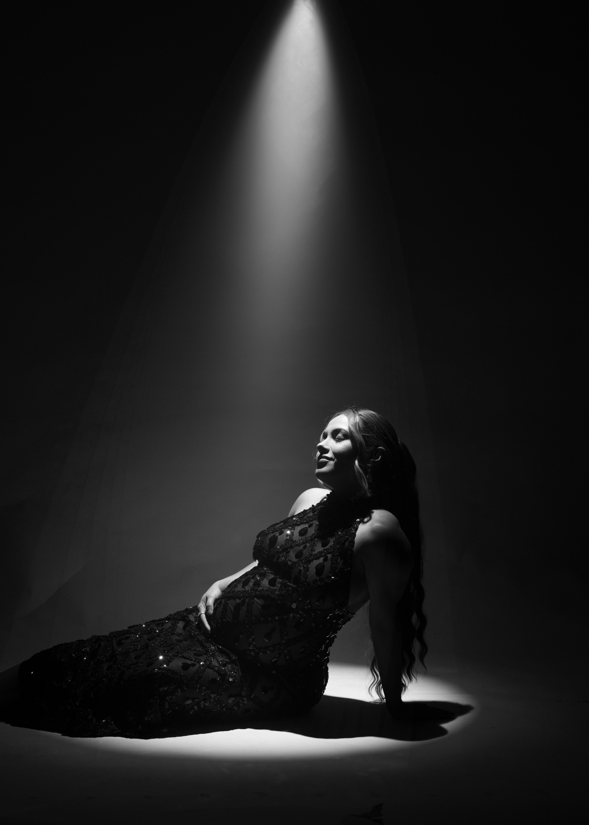 Dramatic black and white maternity portrait under a spotlight, photographed in Dallas, Texas.