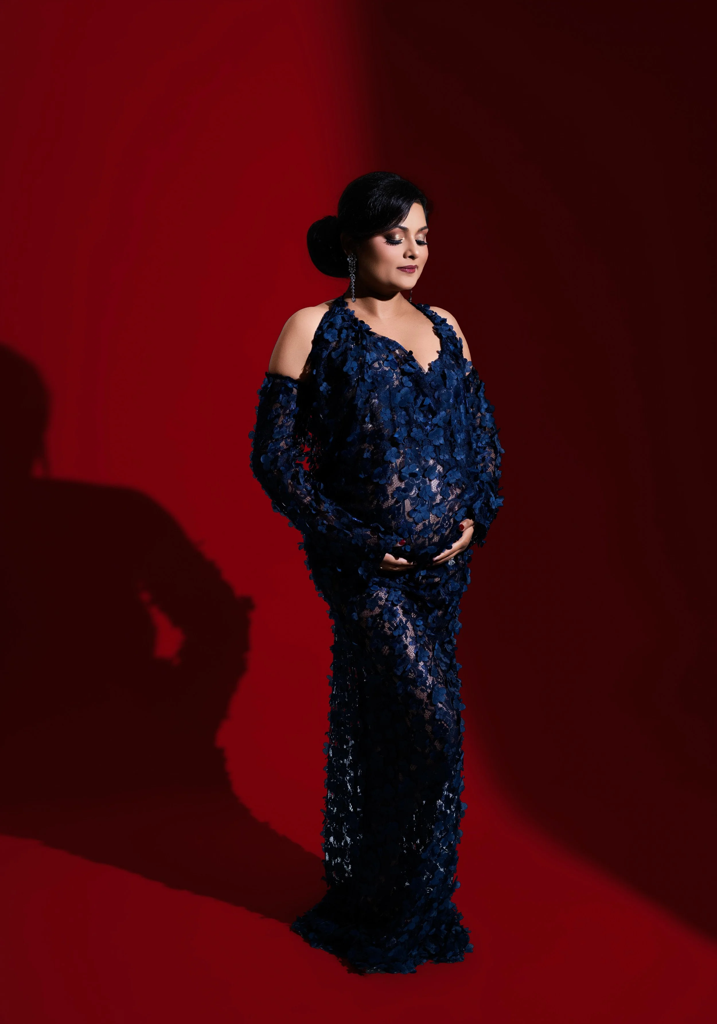 Editorial maternity portrait in a deep blue sequined gown with dramatic red backdrop and lighting, photographed in Dallas, Texas.