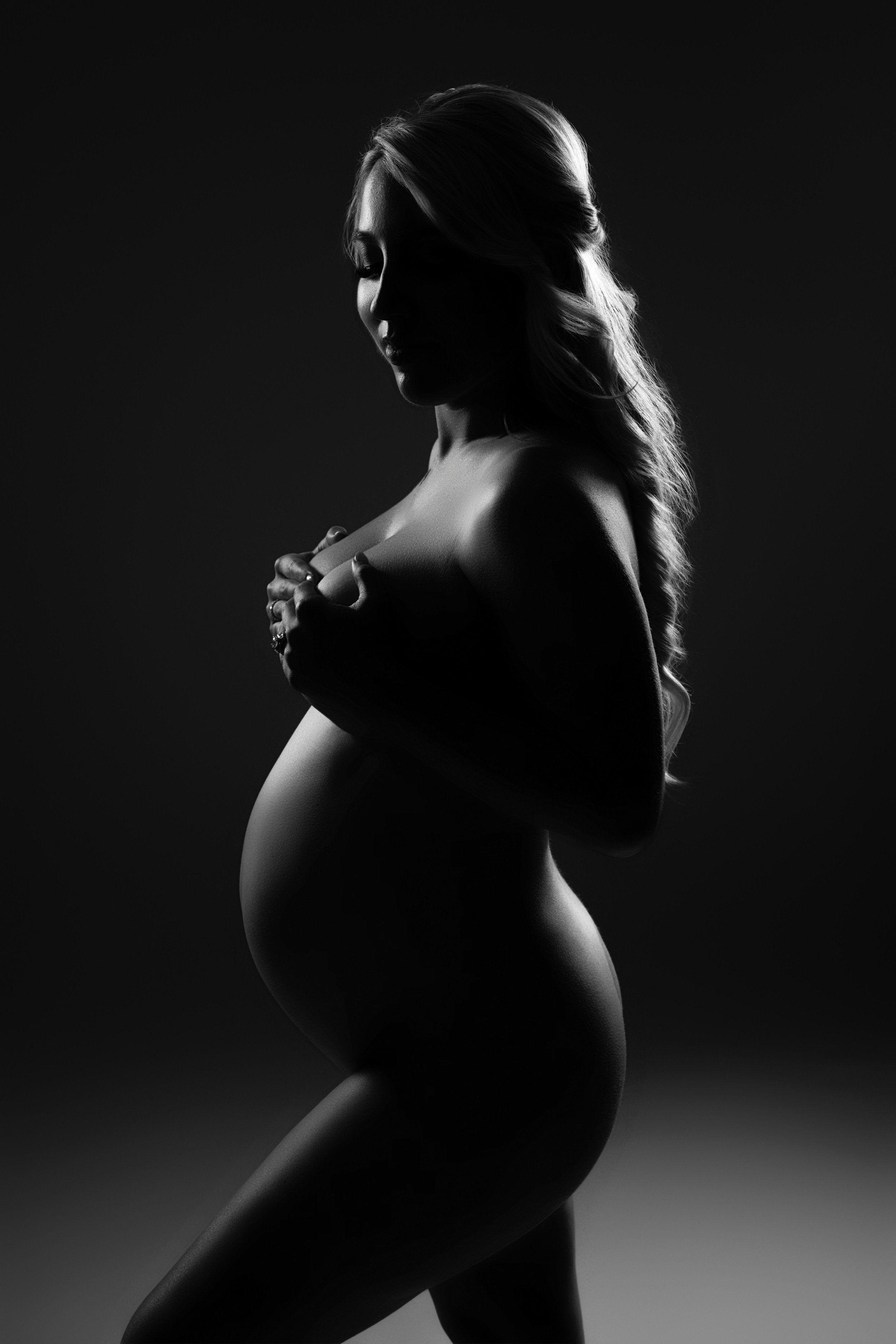 Dramatic black and white maternity silhouette portrait with sculptural studio lighting, photographed in Dallas, Texas.