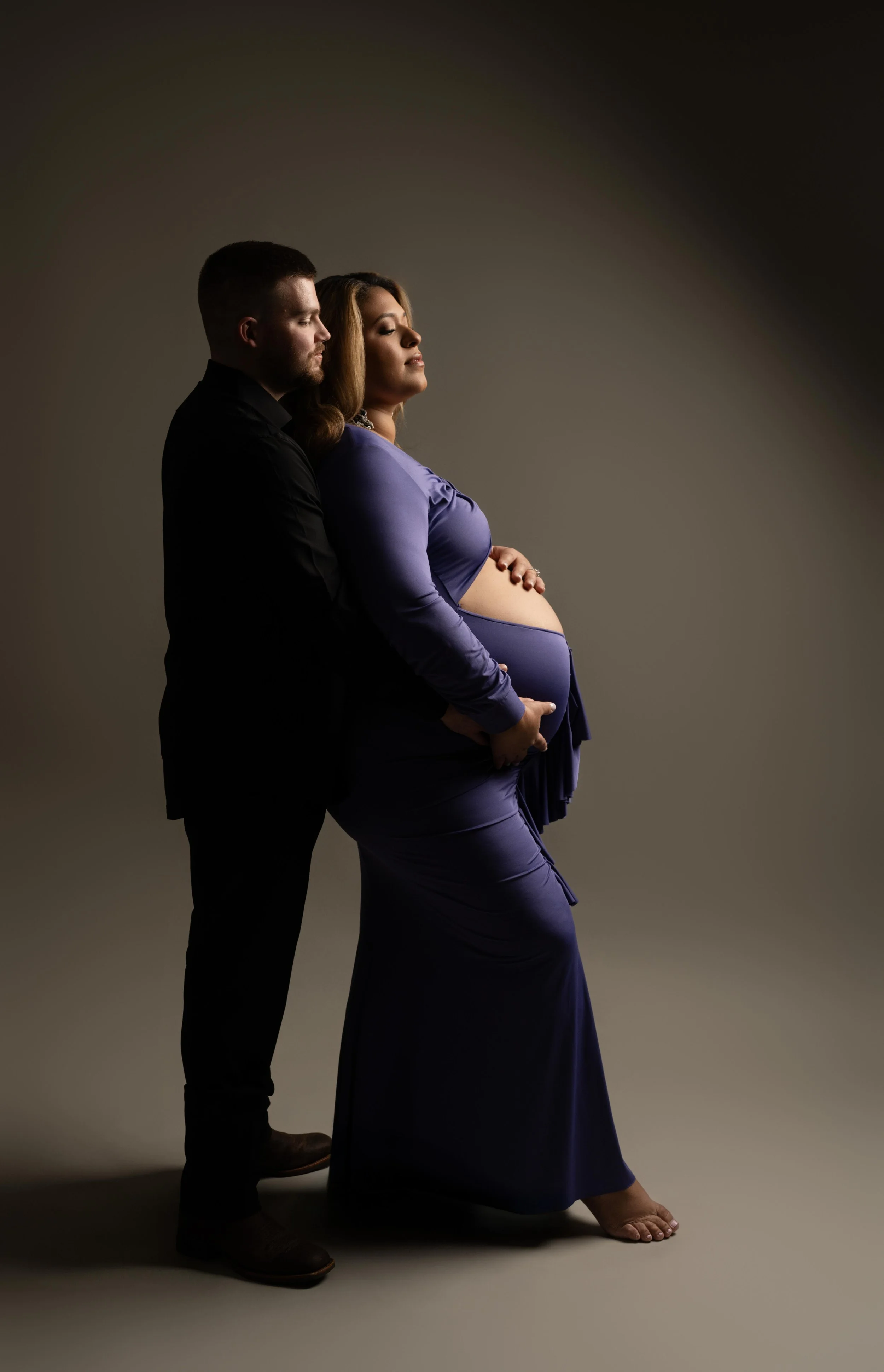 Intimate maternity portrait with partner in a dark studio setting, photographed in Dallas, Texas.