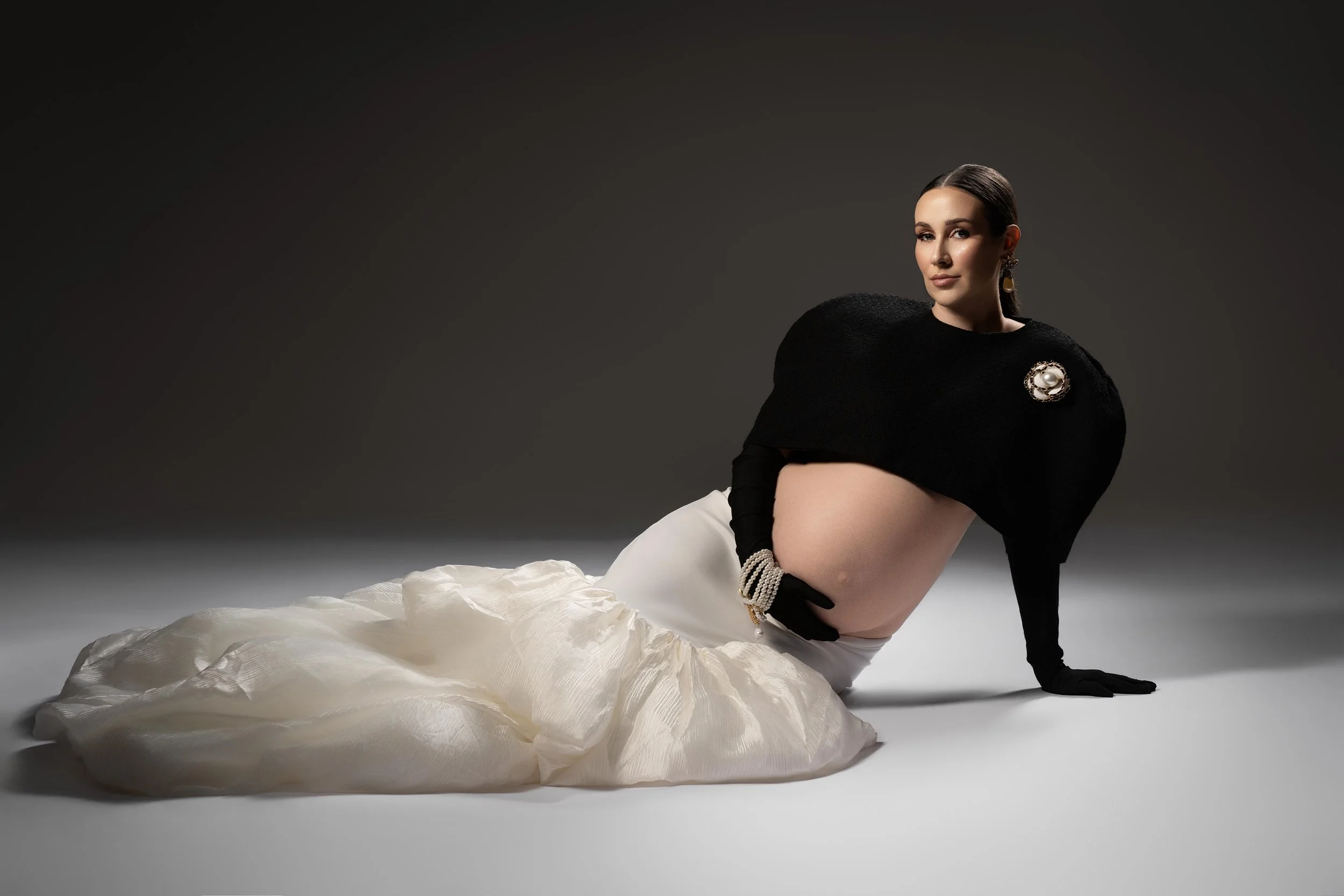 Fashion-forward maternity portrait in a Dallas-area studio featuring a pregnant woman posed in a black top and flowing white skirt.