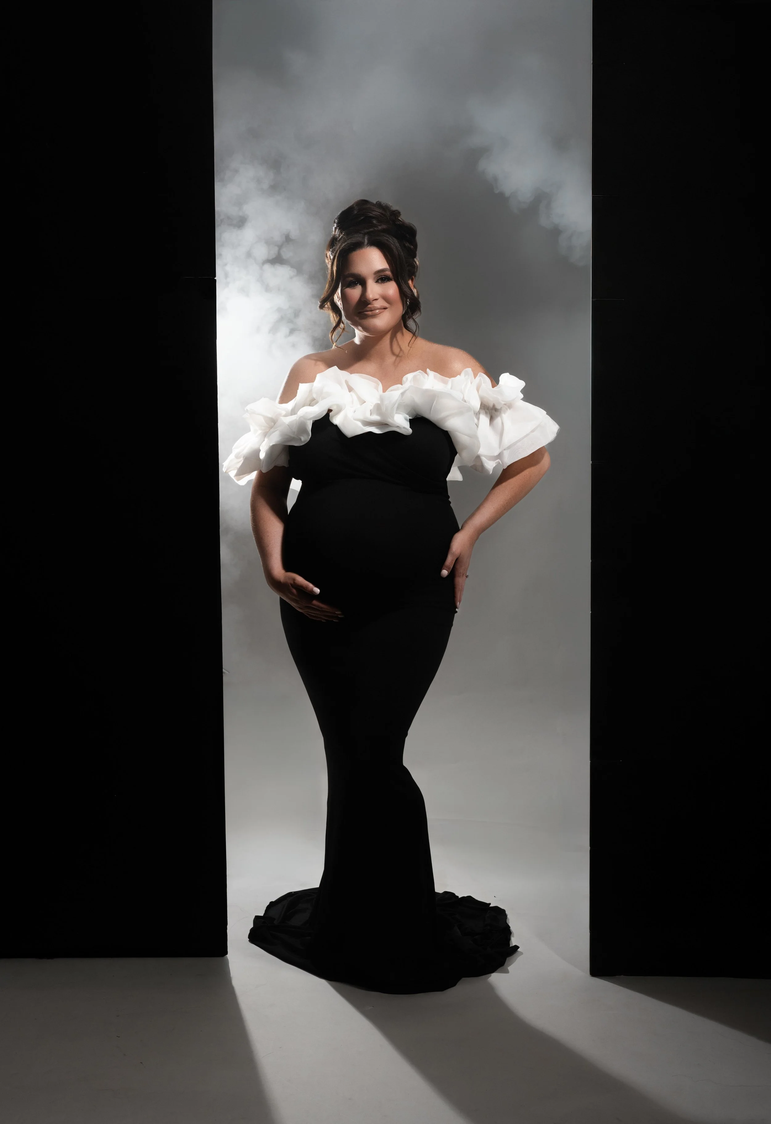 Dramatic maternity portrait in a black gown with sculptural white ruffles and editorial studio lighting, photographed in Dallas.