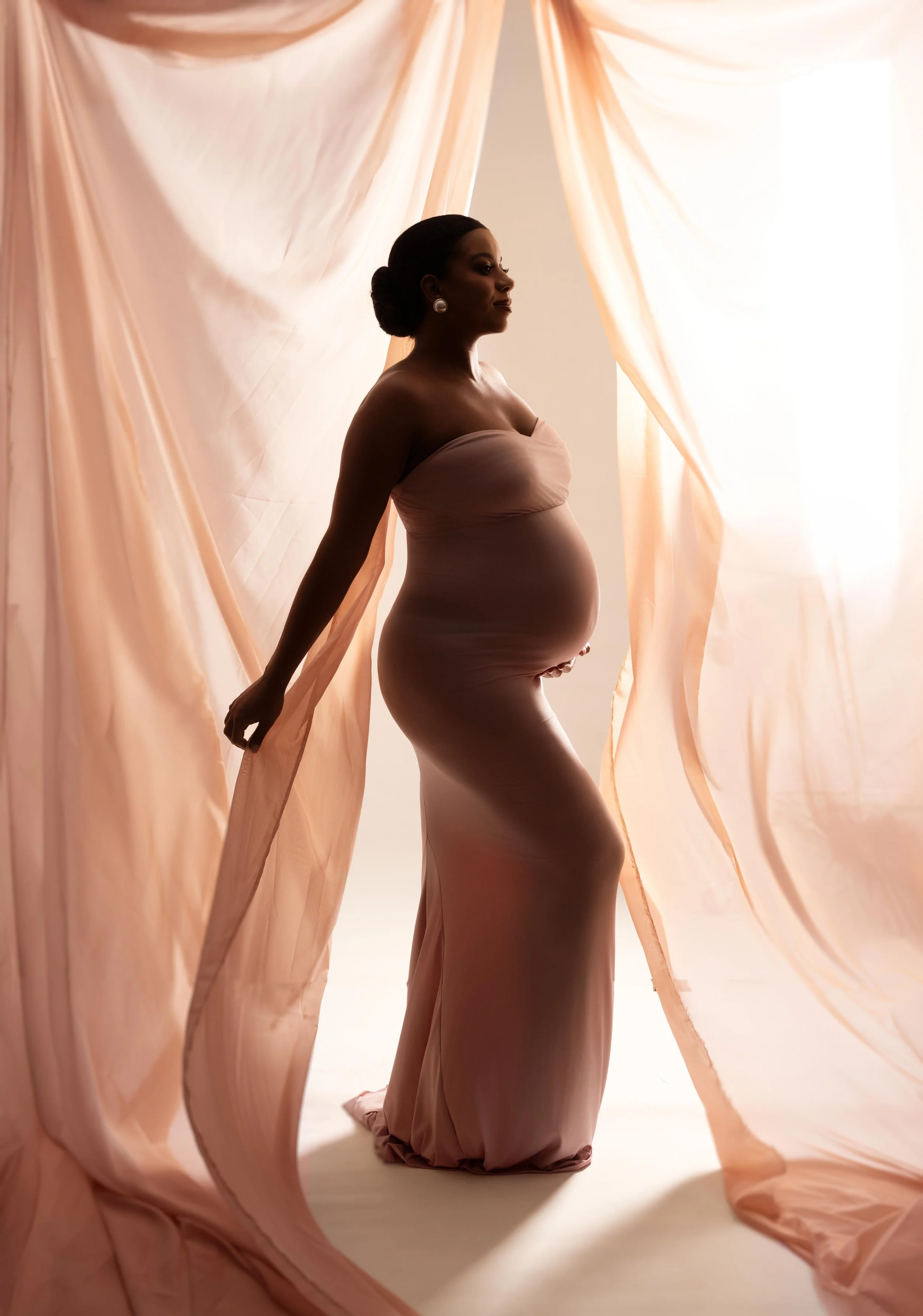 Dallas maternity portrait featuring a mother-to-be surrounded by softly draped fabric and warm, romantic backlighting.