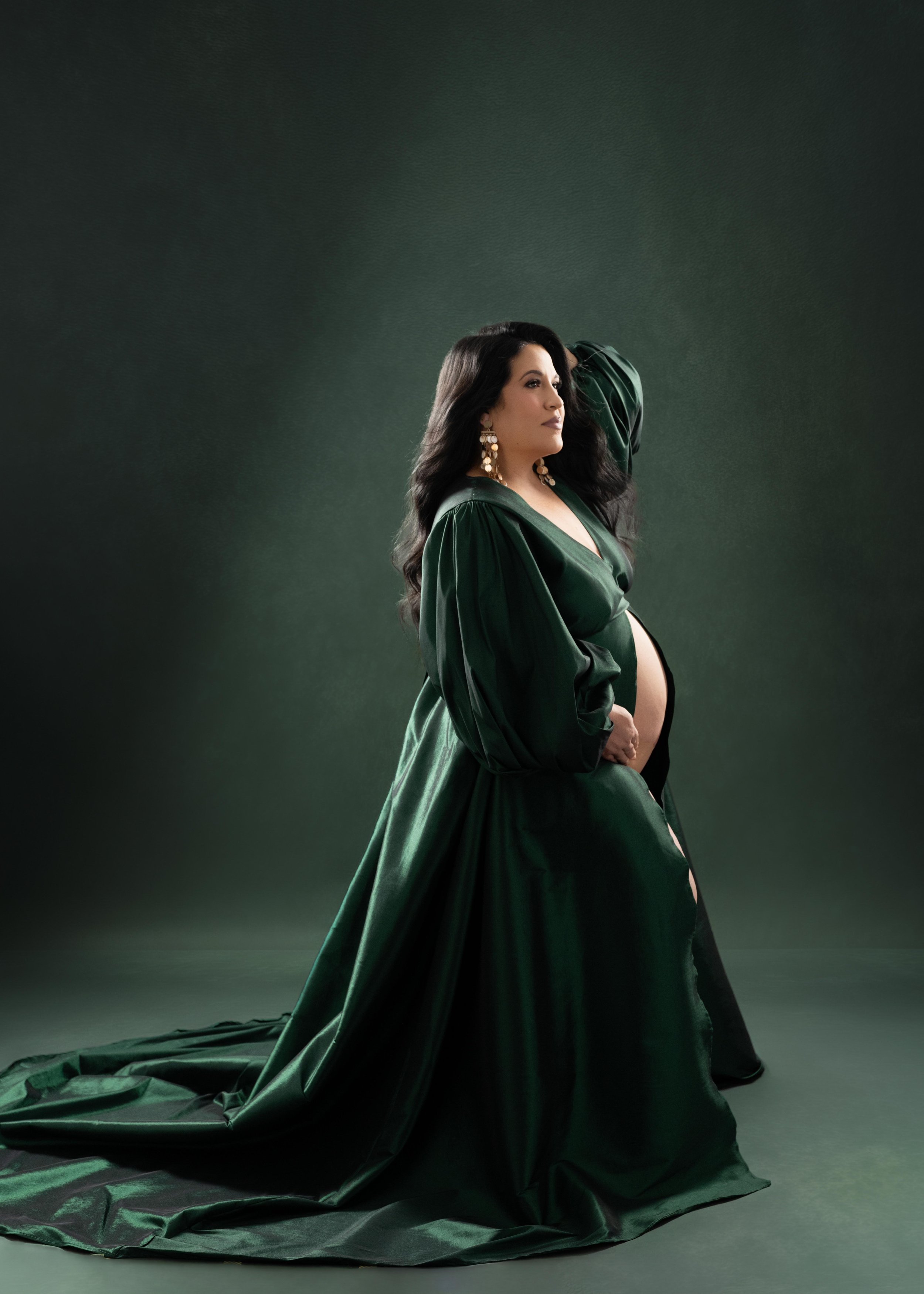 Elegant maternity portrait in an emerald green gown with dramatic studio lighting, photographed in Dallas, Texas.