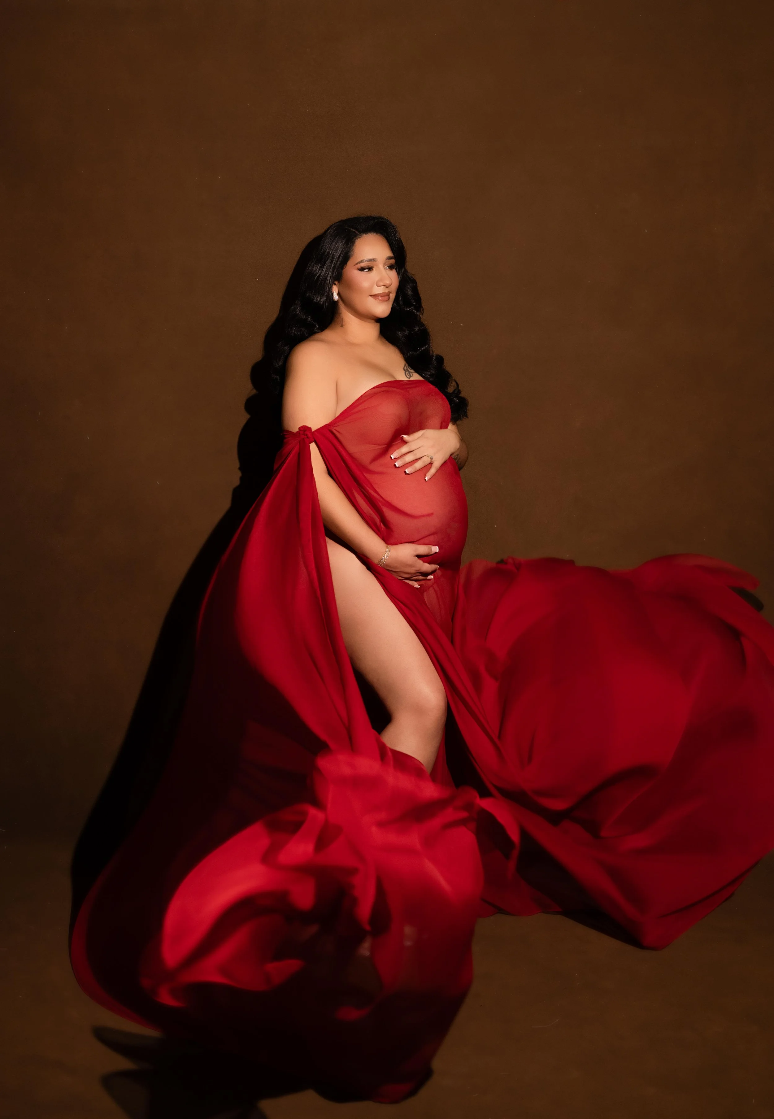 Editorial maternity portrait in a dramatic flowing red gown with warm studio lighting, photographed in Dallas.