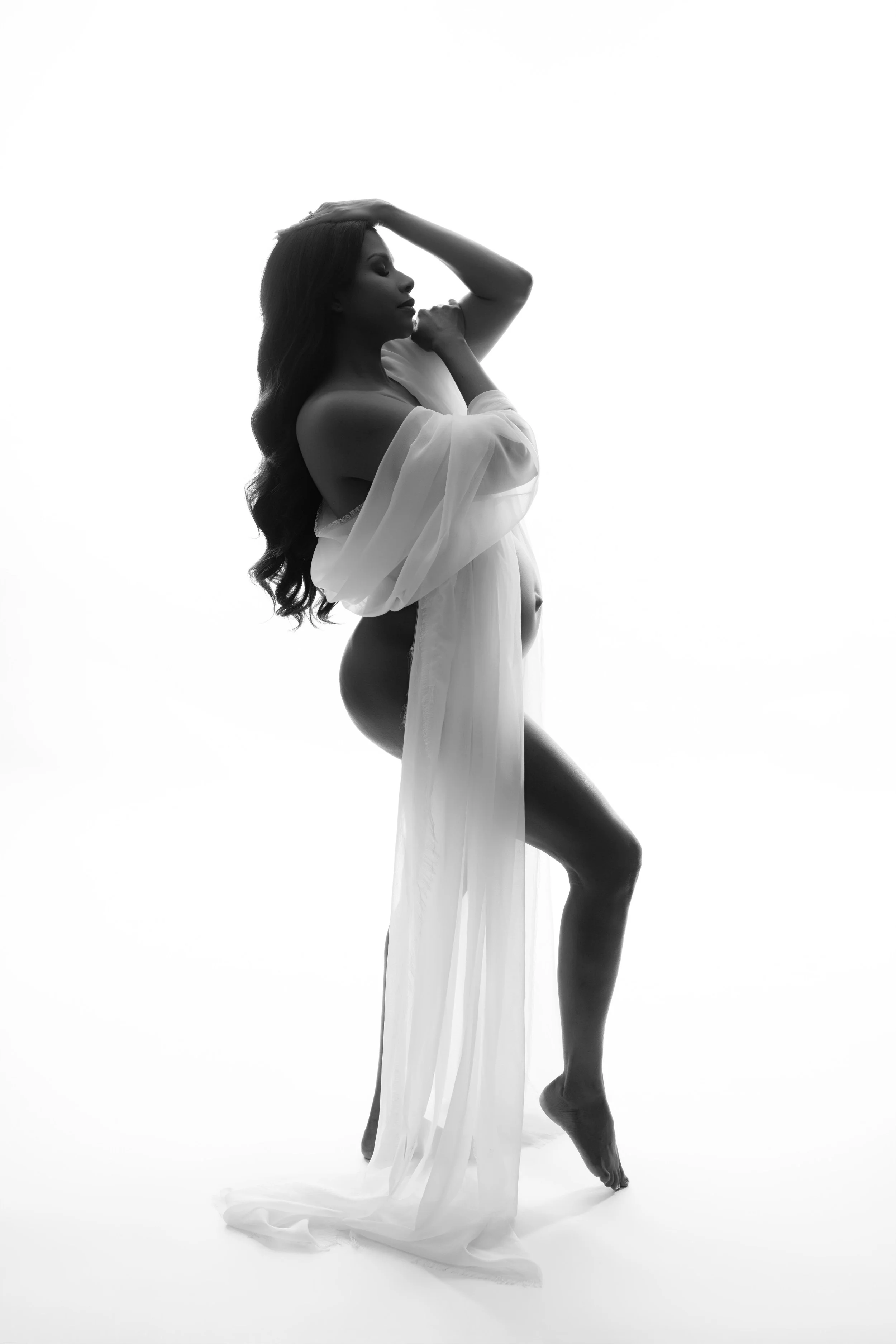 High-key black and white studio maternity portrait with flowing sheer fabric, photographed in Dallas.