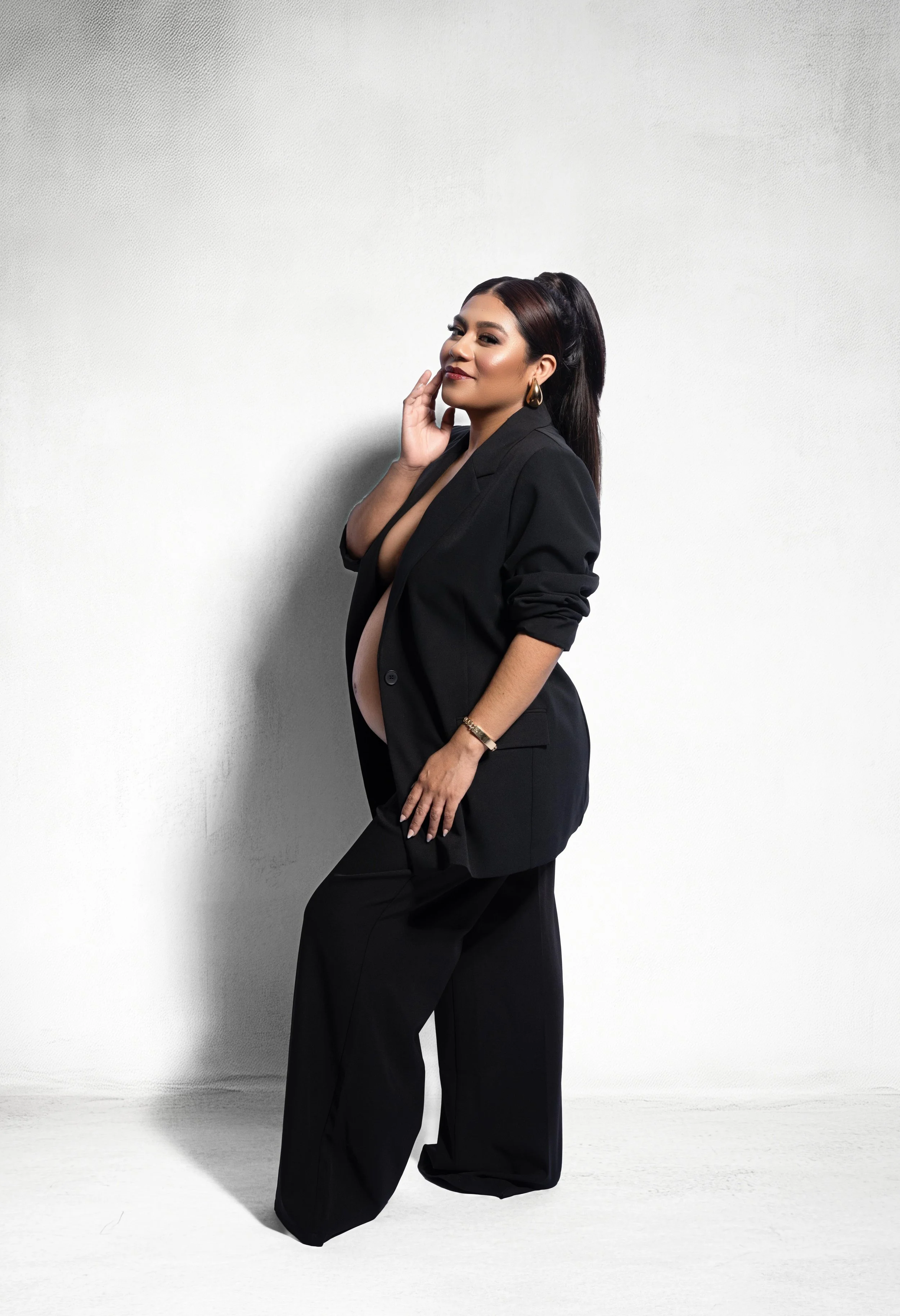 Fashion-inspired maternity portrait in a black suit with exposed baby bump, photographed in a Dallas, Texas studio.