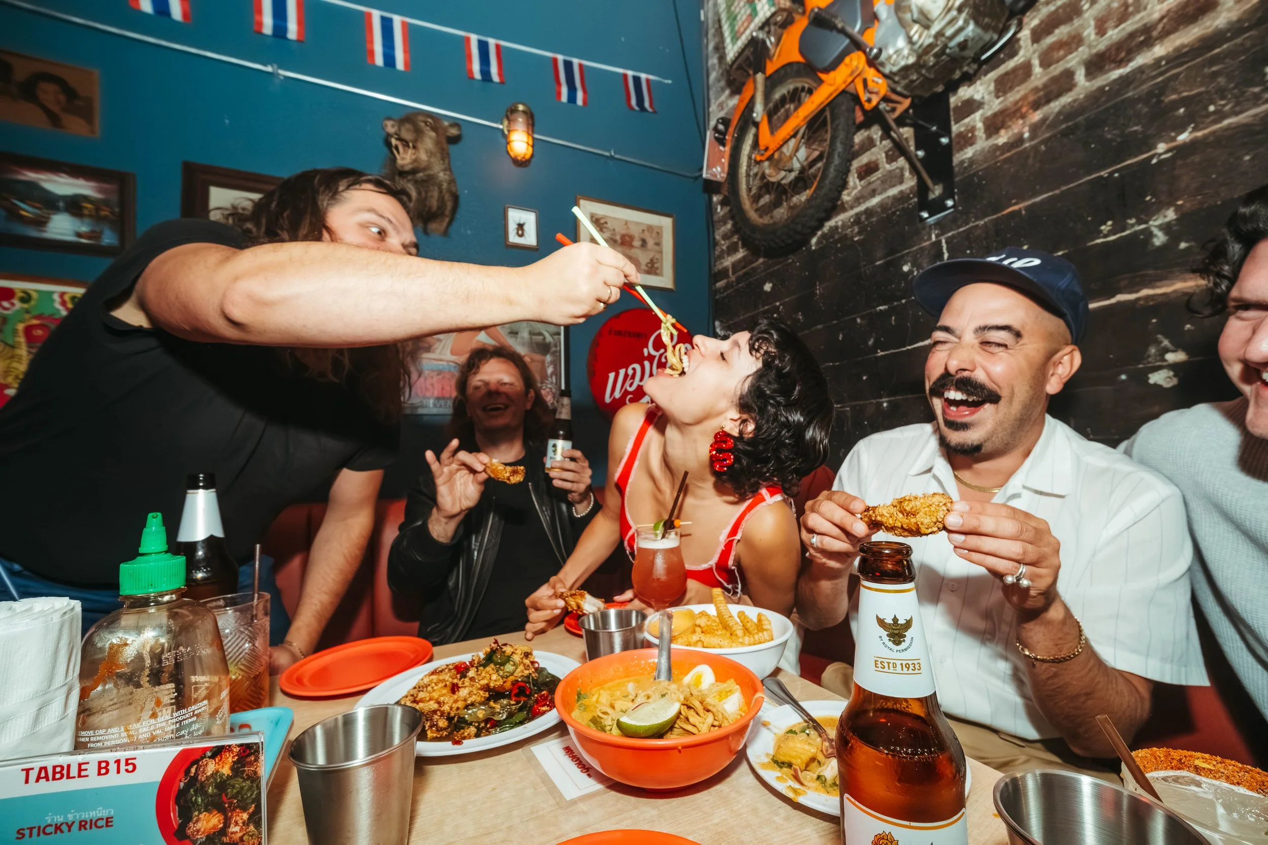 a group of friends laughing and enjoying thai food in a colorful space