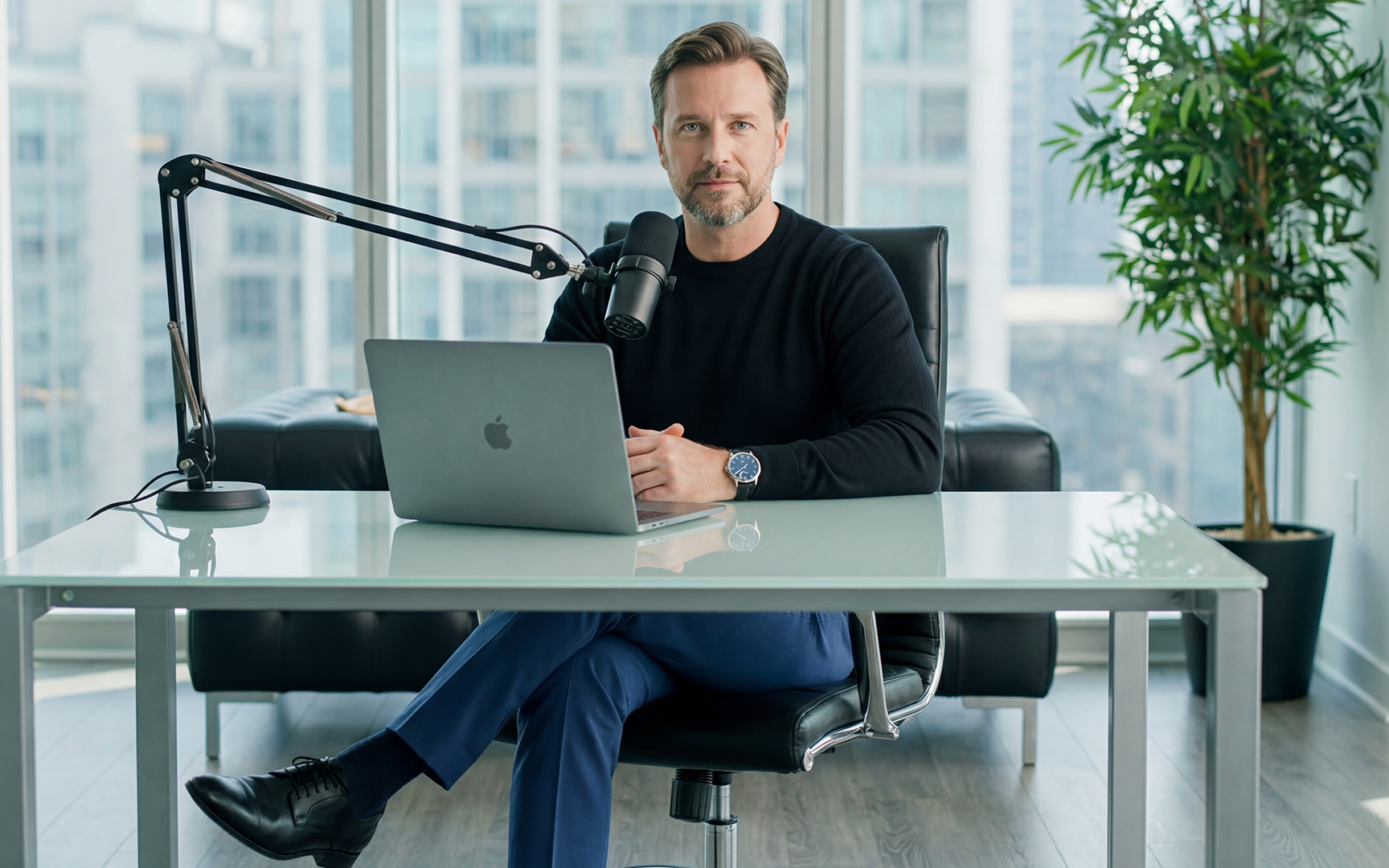 An executive business founder sitting at a modern desk recording a premium podcast interview, showcasing corporate authority solutions by The Expert Bookers.