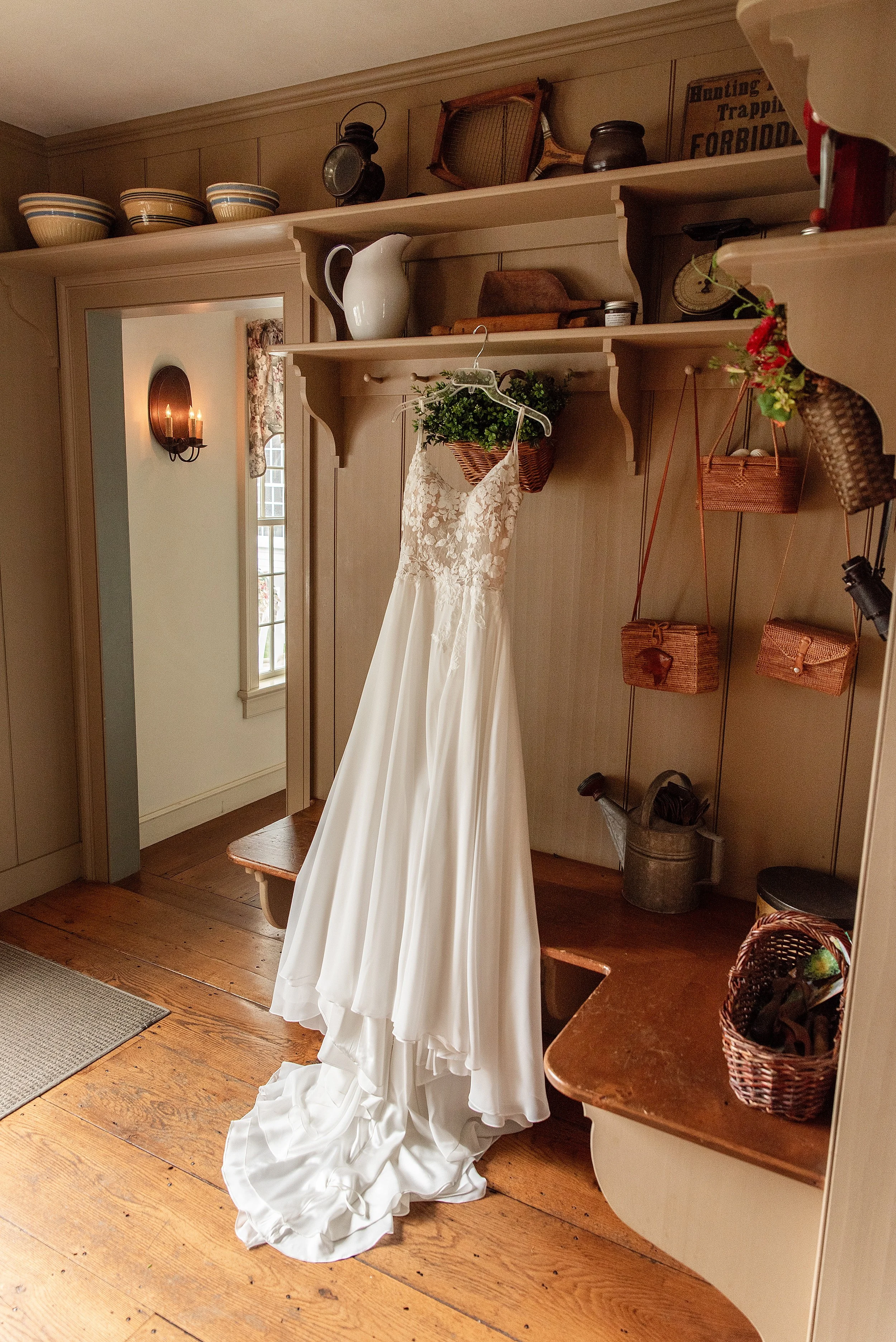 A wedding dress hanging in the farmhouse cottage entryway with wicker baskets and rustic details at Smith Farm Gardens.