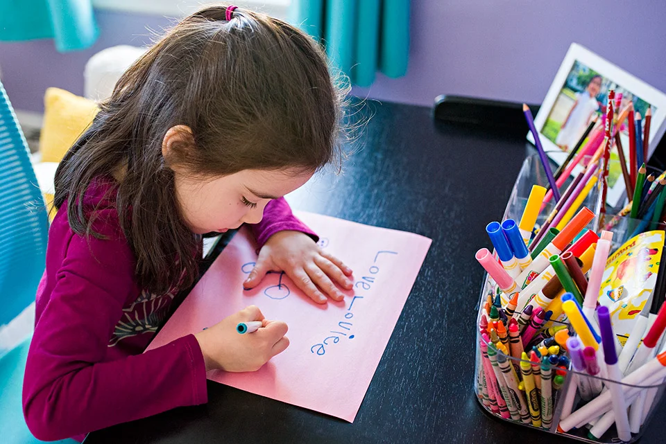 girl coloring on pink paper with blue marker on desk west hartford connecticut documentary family photography