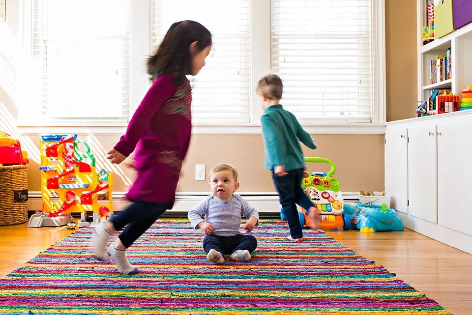 brother and sister running in circles around baby sister in playroom west hartford connecticut family documentary photography