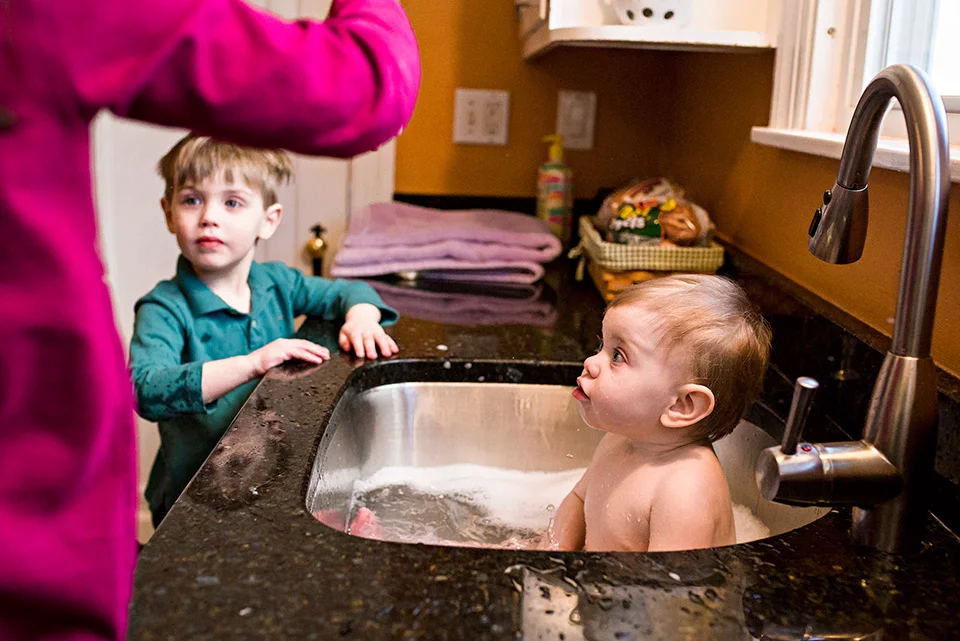 baby taking a bath in kitchen sink while brother helps west hartford ct family documentary photography