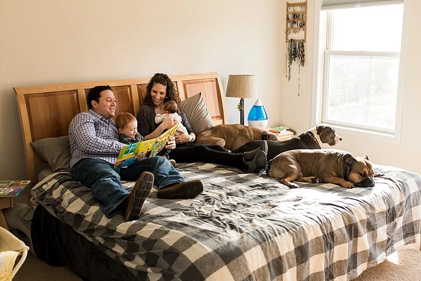 Dad reading books to son in bed during at home newborn photography session in Connecticut.