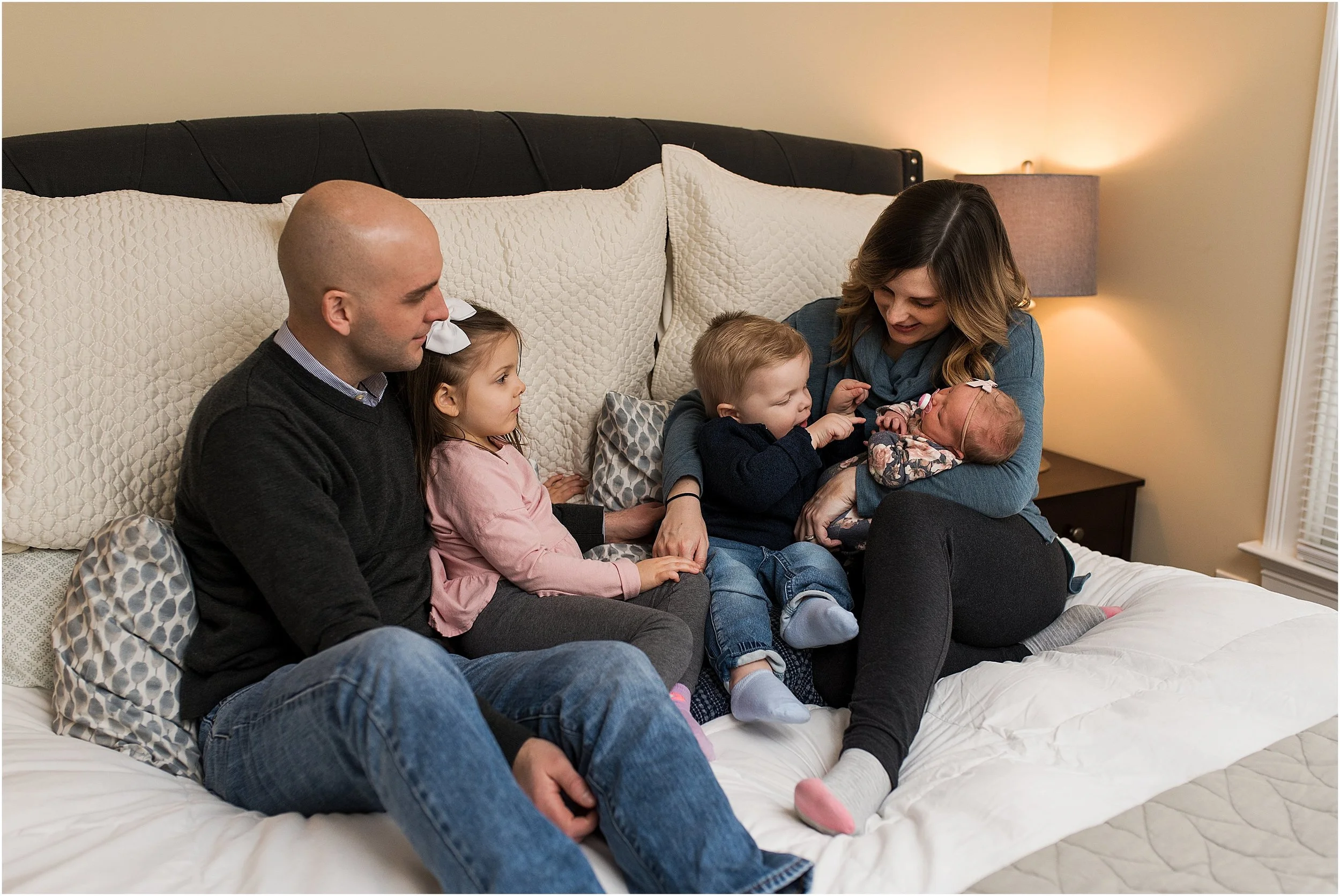 Kids snuggled up in bed with mom and dad and newborn sister.