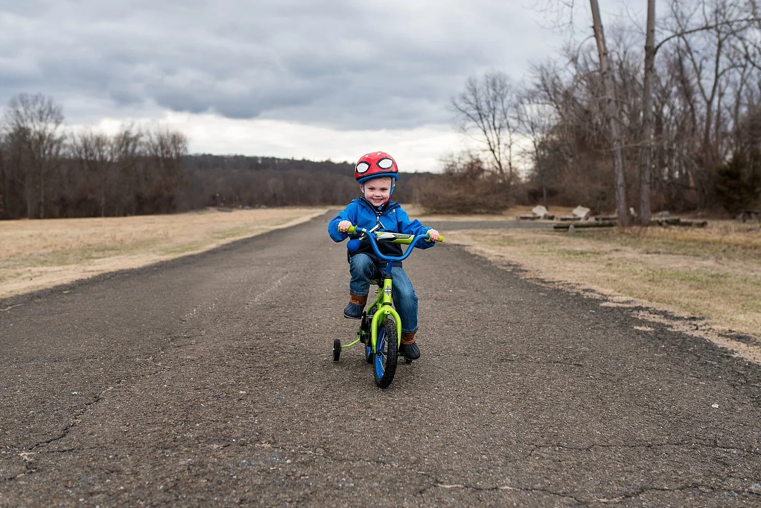 toddler boy in blue jacket riding green bike during ct professional family photos
