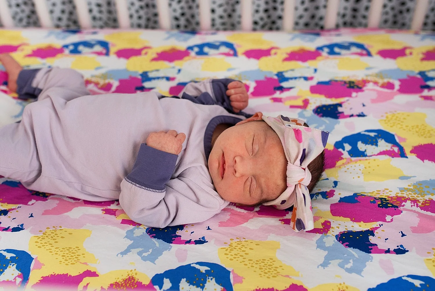 Baby girl laying in her crib with her colorful crib sheets. Newborn photography CT