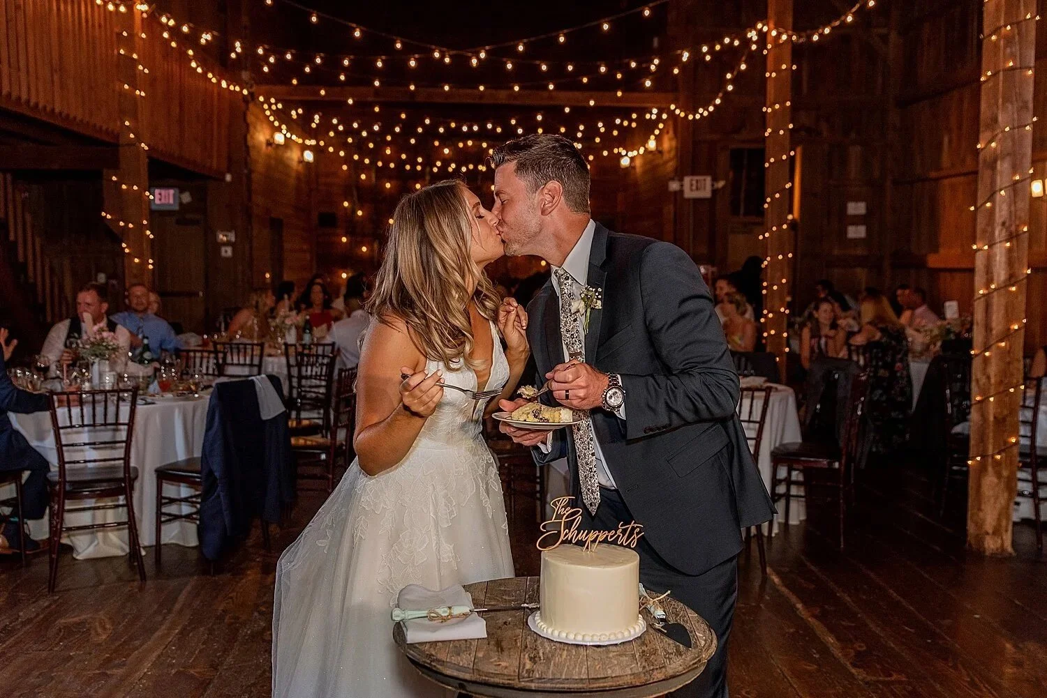 Cake cutting with string lights in back inside barn wedding connecticut