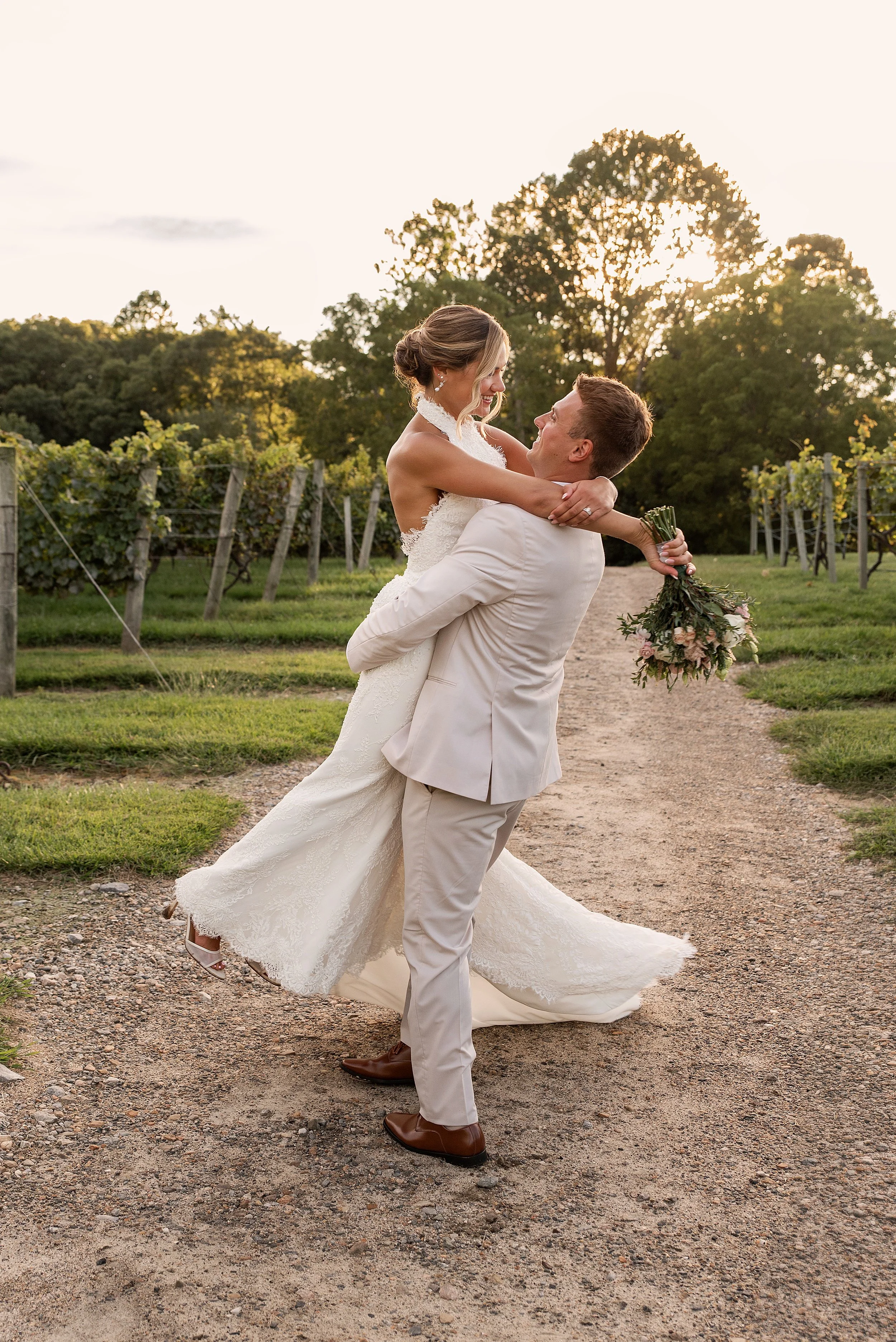A romantic sunset portrait of a groom lifting and spinning his bride in front of a glowing vineyard background.