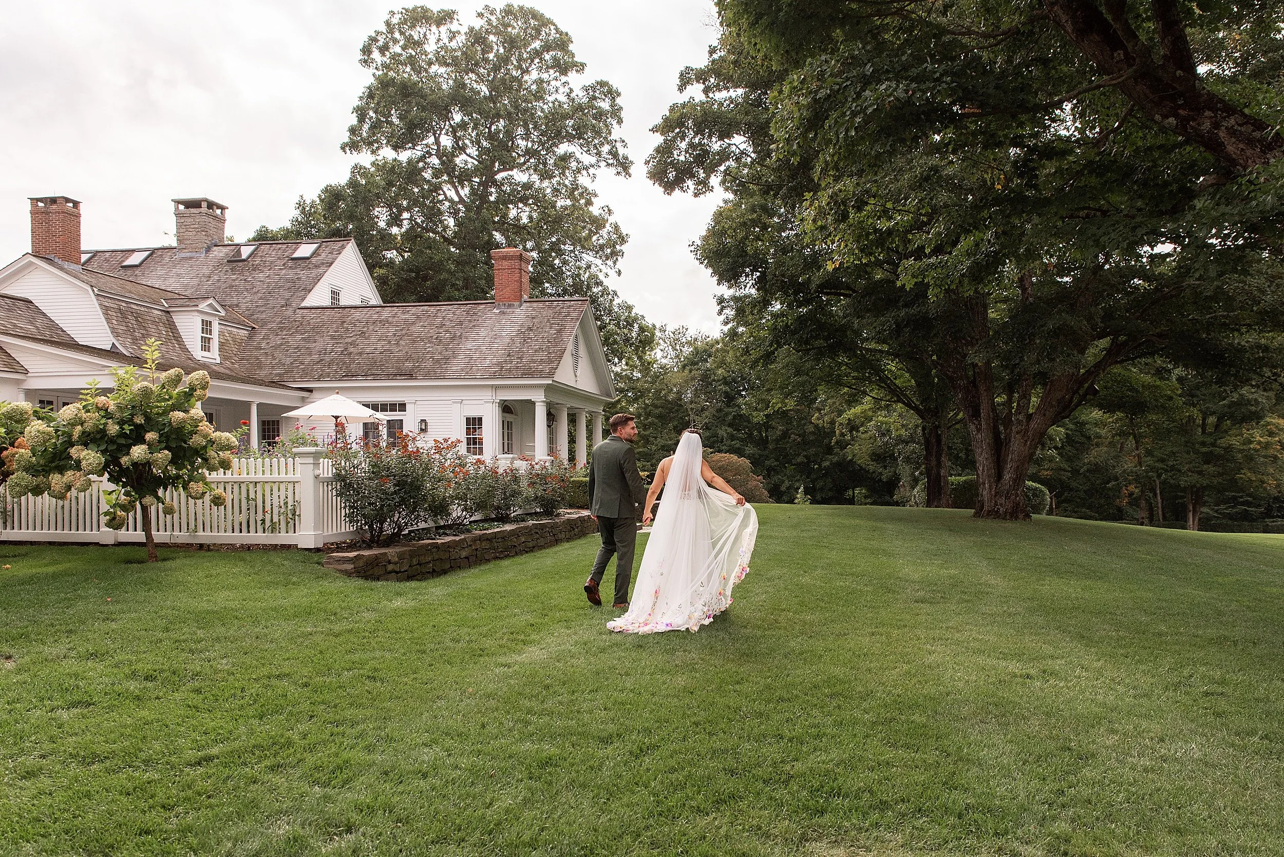 A wedding couple holding hands and walking through the expansive back lawn and property of a private Connecticut estate venue.