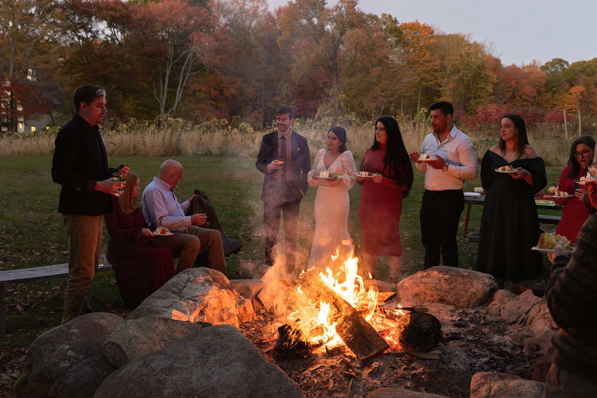 Bride and groom having cake around the fire pit during small wedding reception in Connecticut captured by small and mid size wedding photographer CT Rebecca Lynne