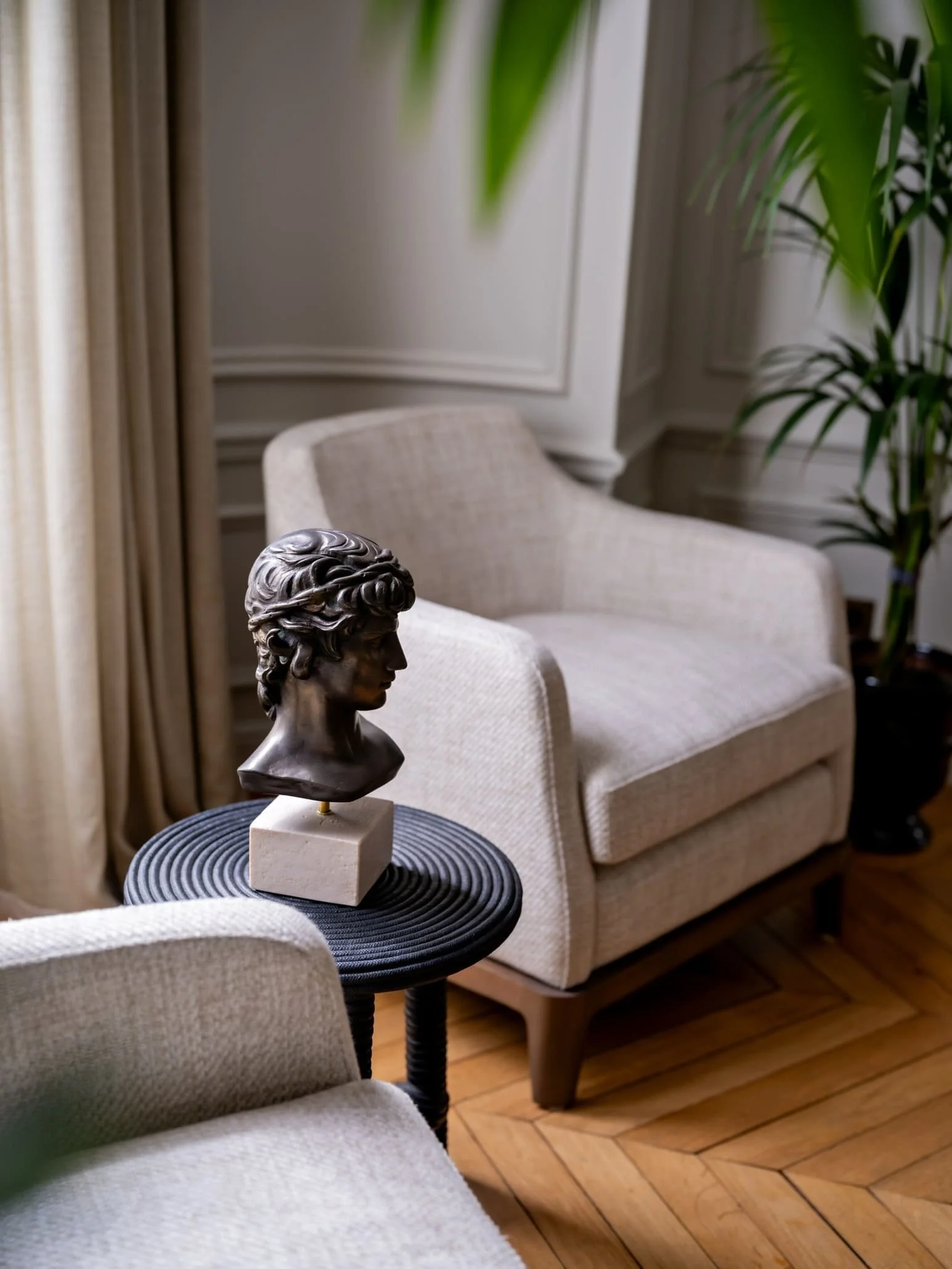 Parisian interior design studio living room with linen armchairs, herringbone parquet floor, and bronze classical bust on a sculptural side table