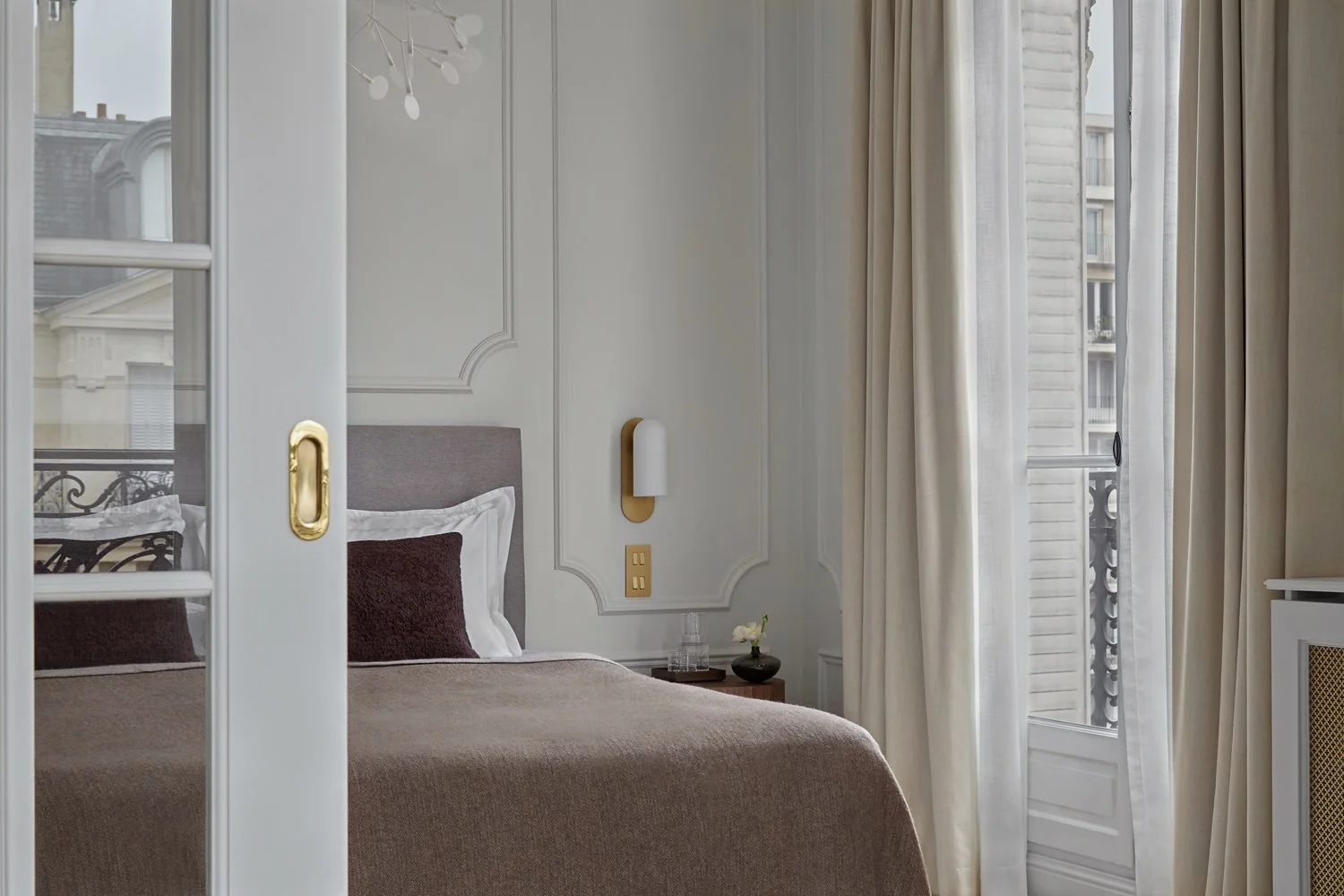 View of an elegantly decorated bedroom. In the center, a bed, and to the right a window overlooking Paris.