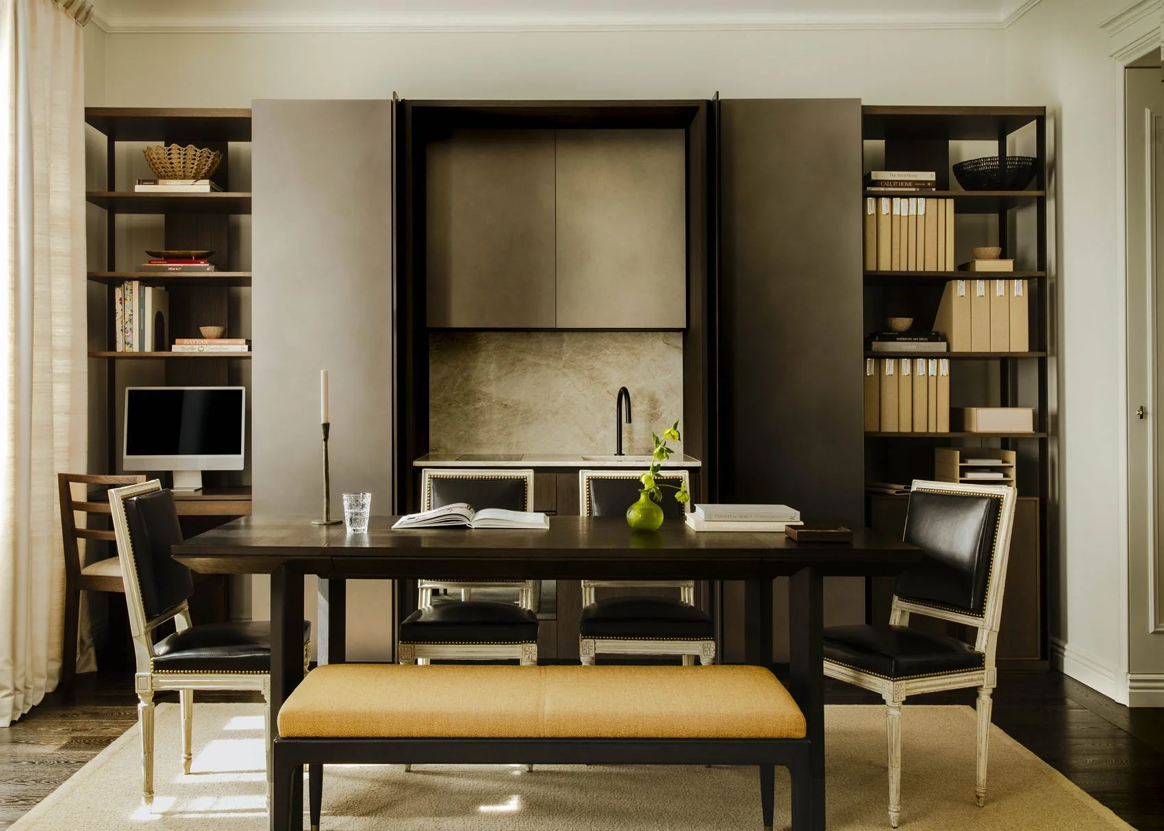 Parisian home office with dark wood built-in shelving, large desk, leather chairs and mustard upholstered bench
