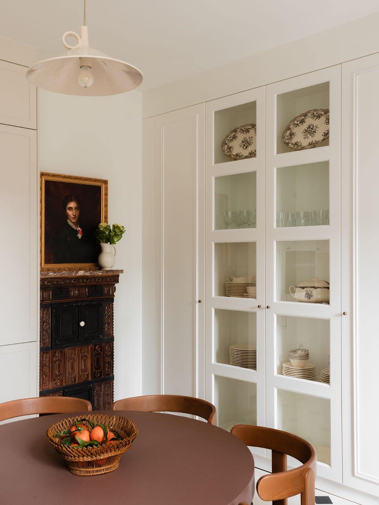 Elegant dining space near Musée d’Orsay with round wood table, glass-front cabinetry, vintage fireplace, framed artwork, and soft modern pendant lighting.