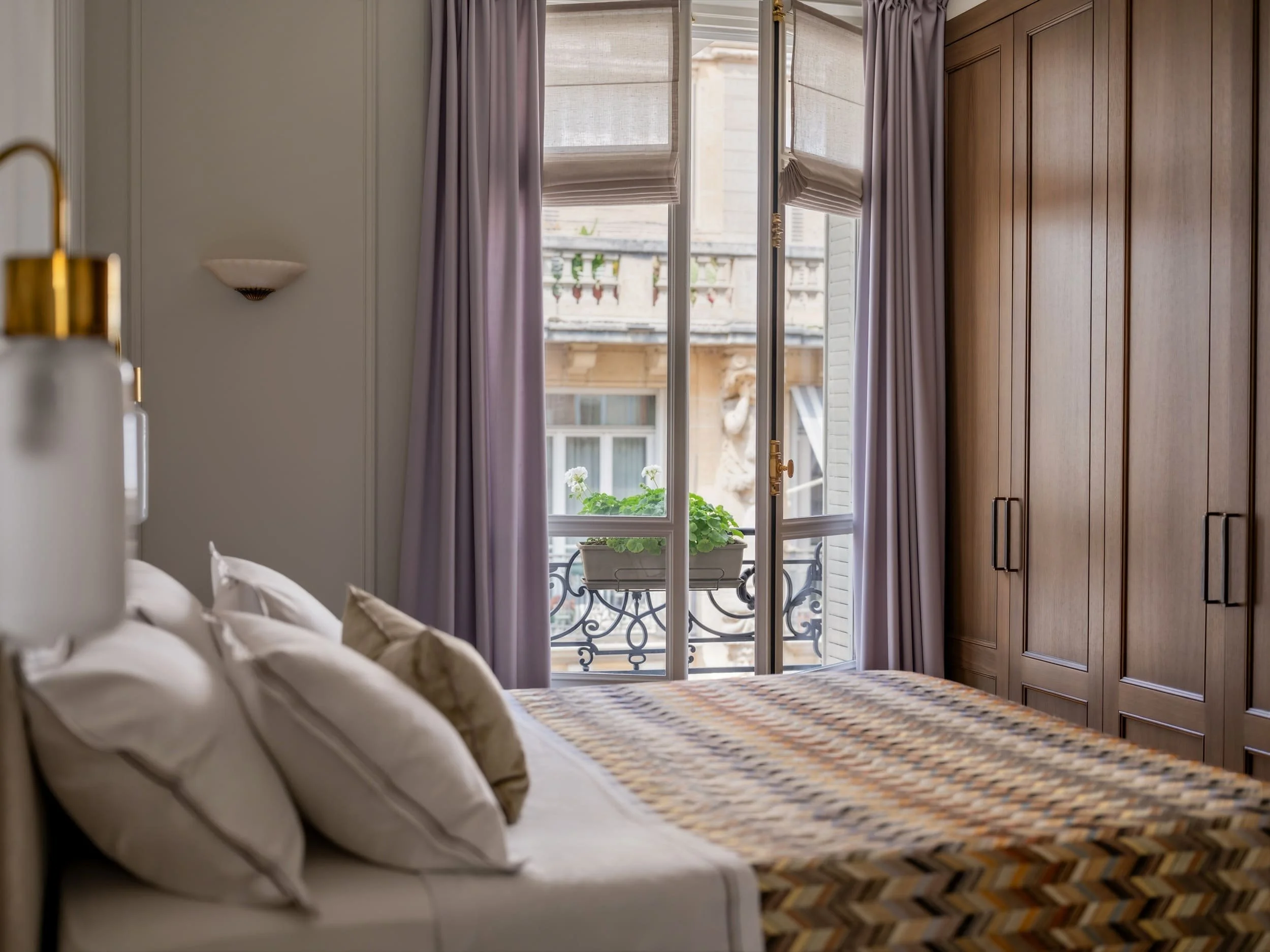 Parisian bedroom with custom walnut wardrobes, lavender silk curtains, French balcony doors and brass wall sconce