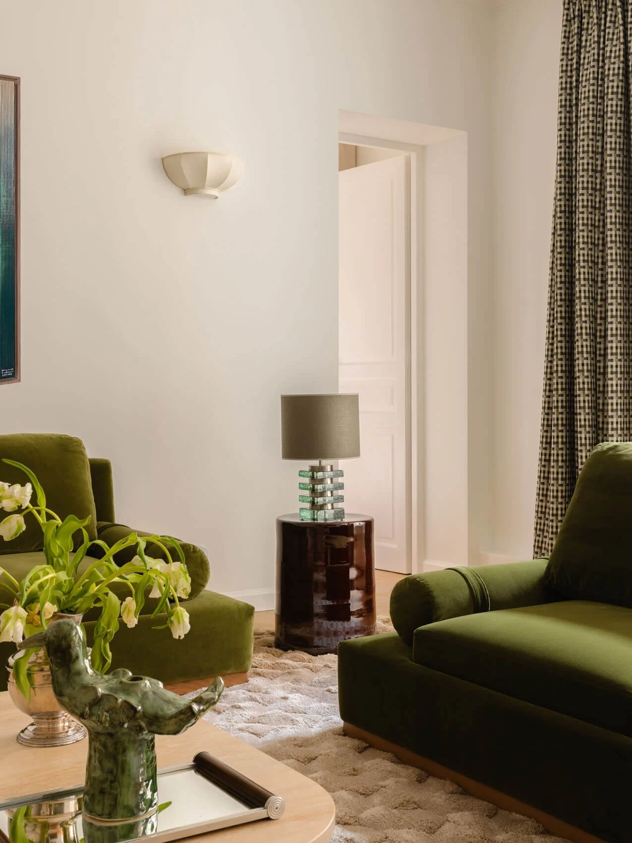 Close-up of Paris apartment living room renovation featuring green velvet armchairs, sculptural side table lamp, neutral walls, and modern interior styling on Rue de Lille.