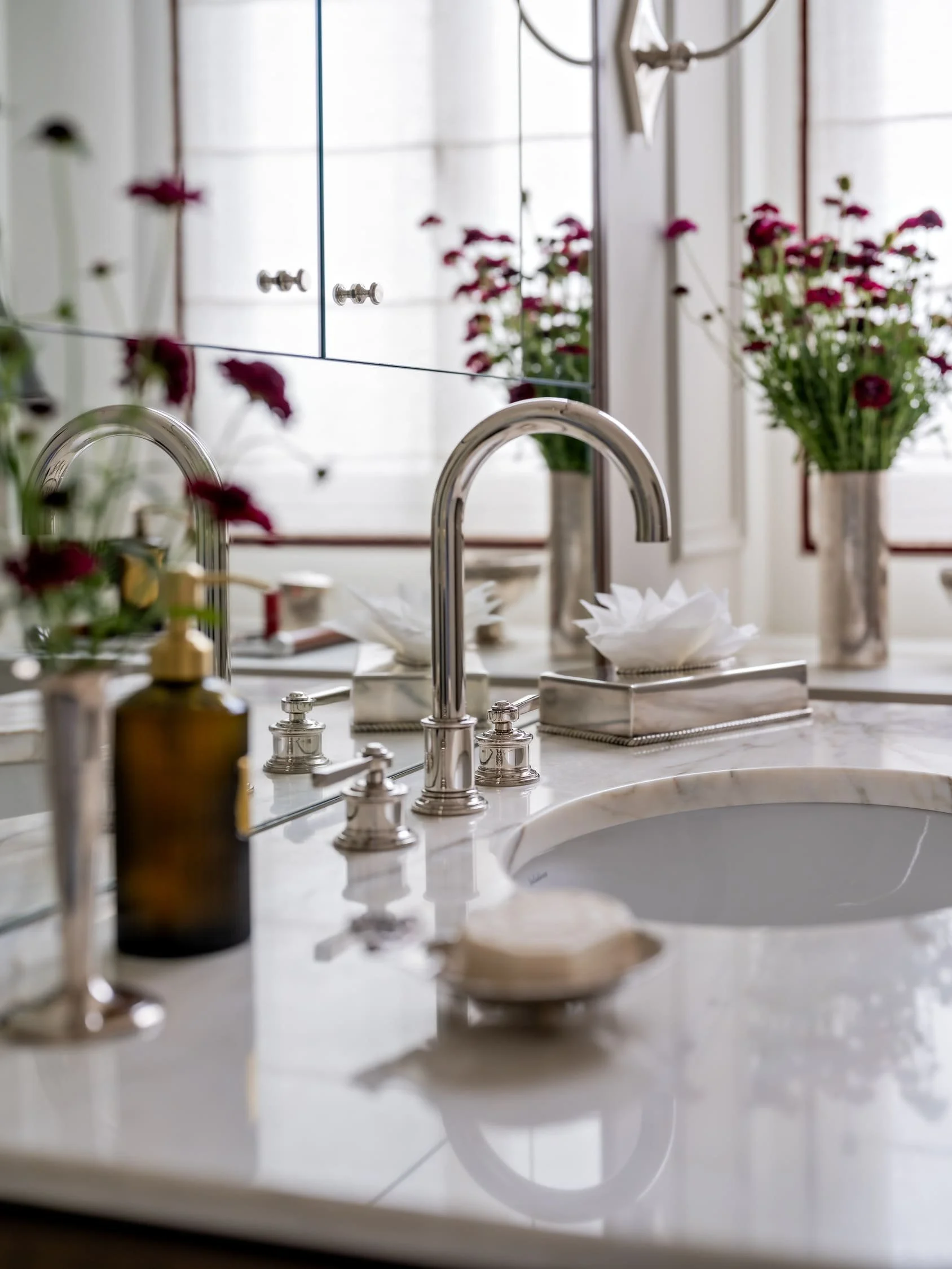 Parisian bathroom vanity detail with marble countertop, polished nickel faucet, mirrored cabinet and fresh burgundy flowers