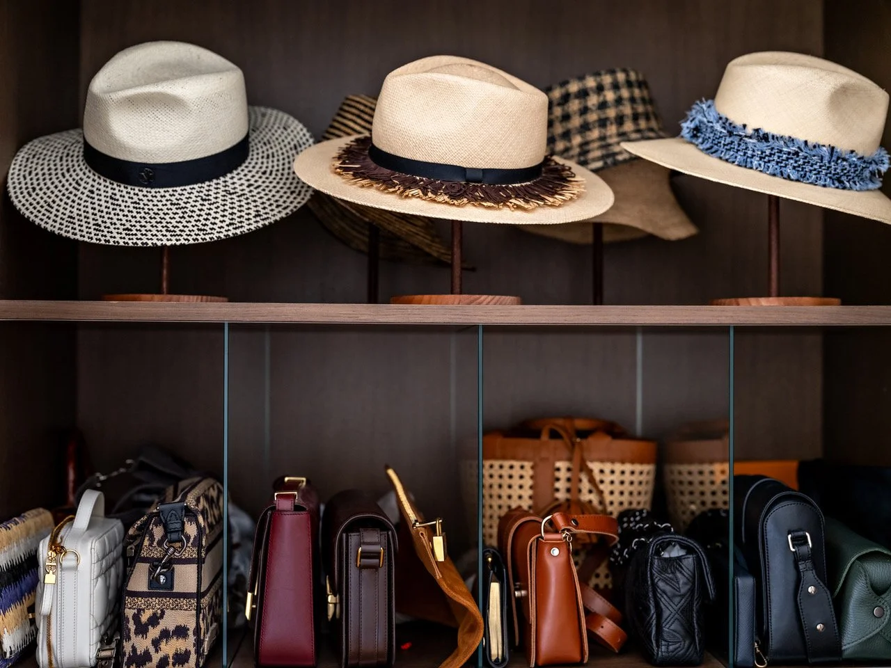 Custom walnut closet in a Paris apartment with summer hats displayed on stands and handbags arranged behind glass-front doors.