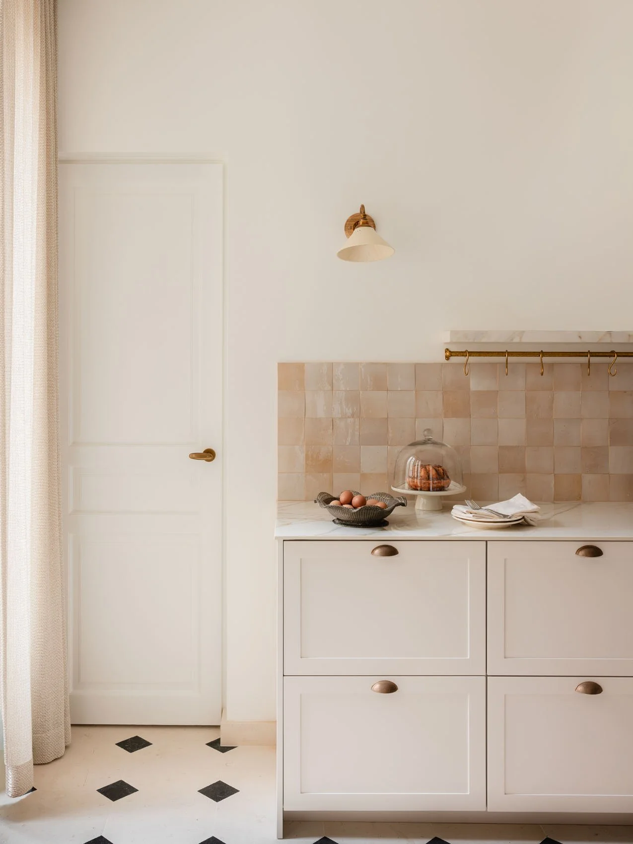 Paris apartment kitchen renovation with custom cabinetry, marble countertop, handmade tile backsplash, brass hardware, vintage wall sconce, and patterned tile flooring.