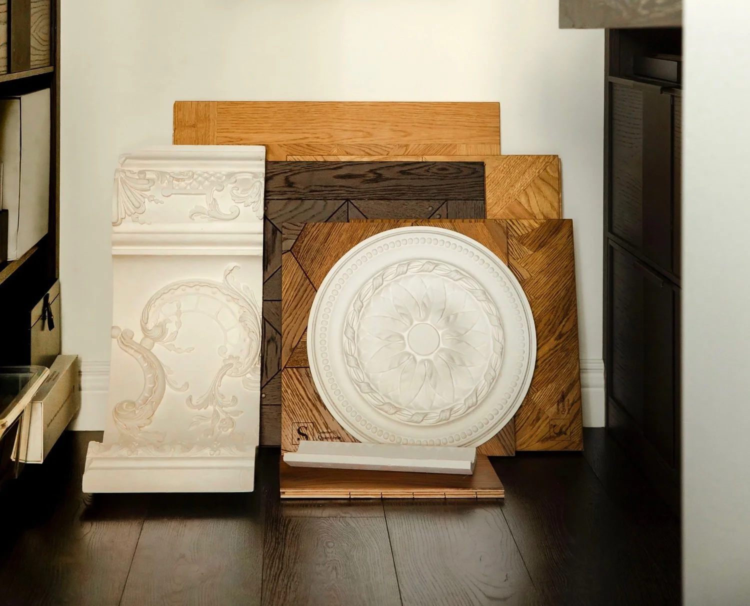 Interior design material samples featuring ornate mouldings and parquet wood panels.