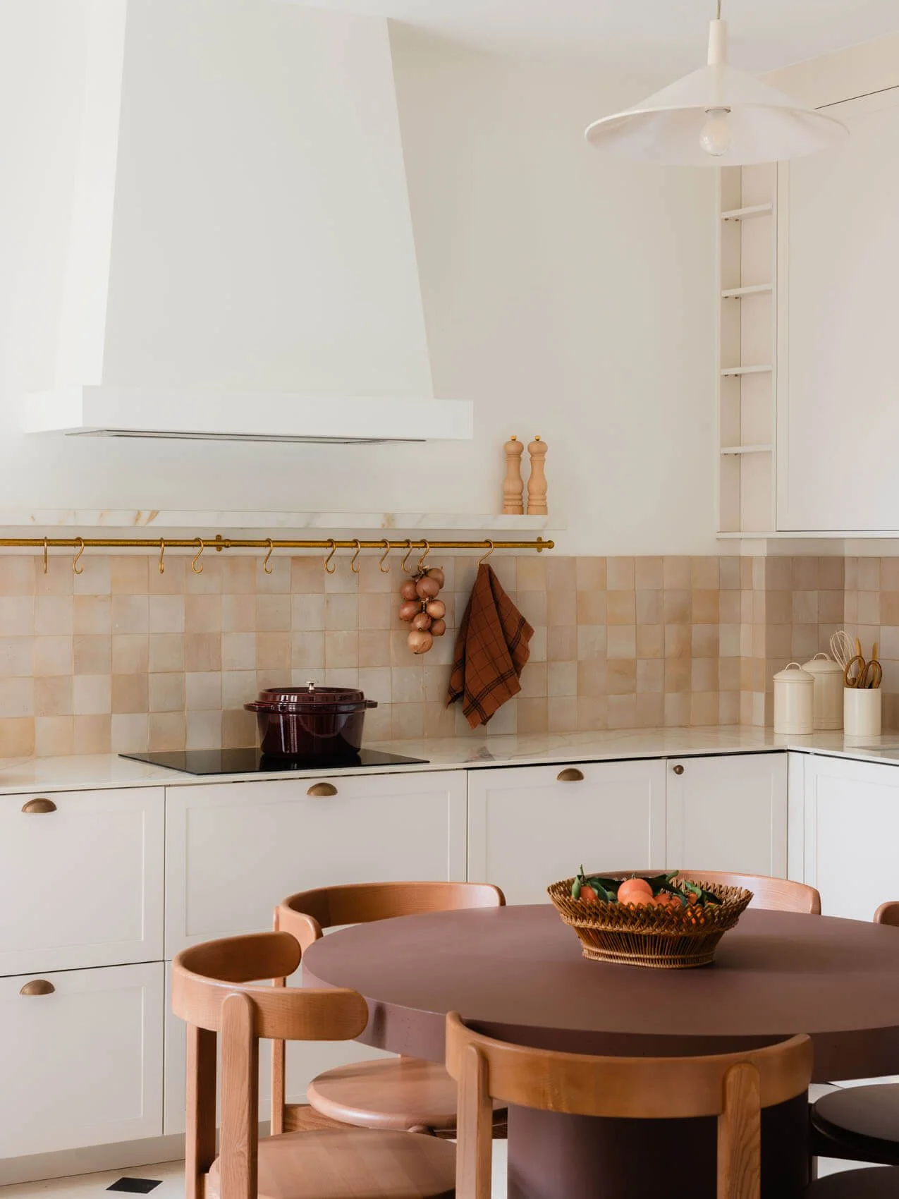 Paris Left Bank apartment kitchen renovation with round dining table, custom white cabinetry, marble countertop, handmade tile backsplash, brass rail detailing, and modern range hood.