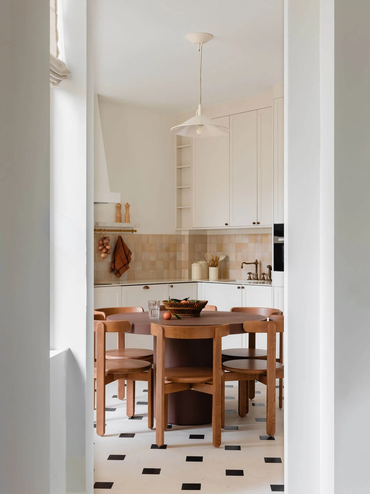 Paris apartment kitchen and dining renovation with round wood table, mid-century style chairs, custom cabinetry, handmade tile backsplash, and patterned tile floor.