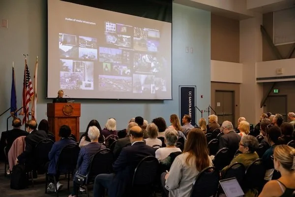 Lisa Parks, Distinguished Professor of Film and Media Studies, delivering her Faculty Research Lecture at UC Santa Barbara on April 10, 2025, with a presentation screen behind her.