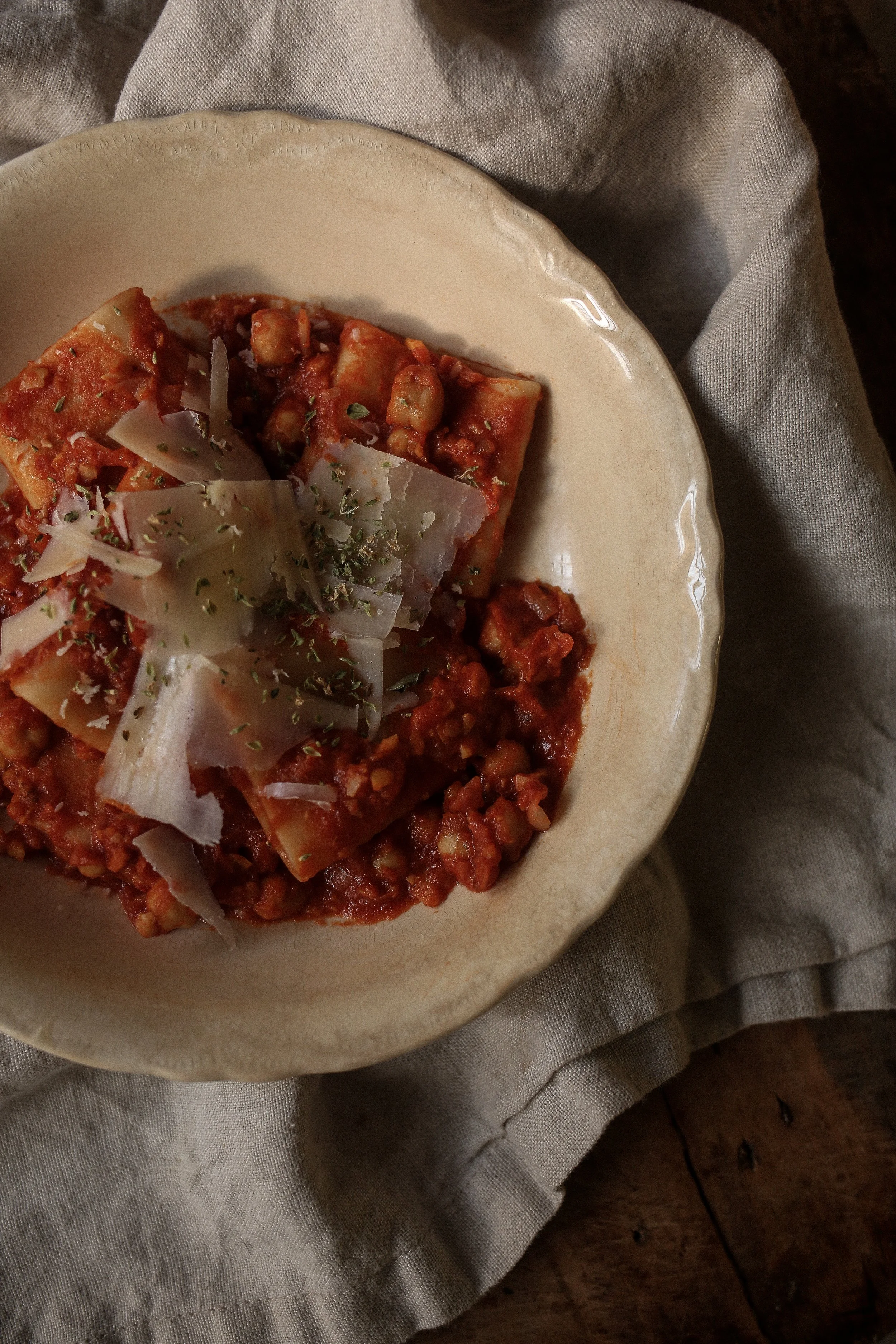 Close-up bowl of pasta with chickpeas showing tender chickpea tomato sauce, al dente pasta and shaved parmesan cheese