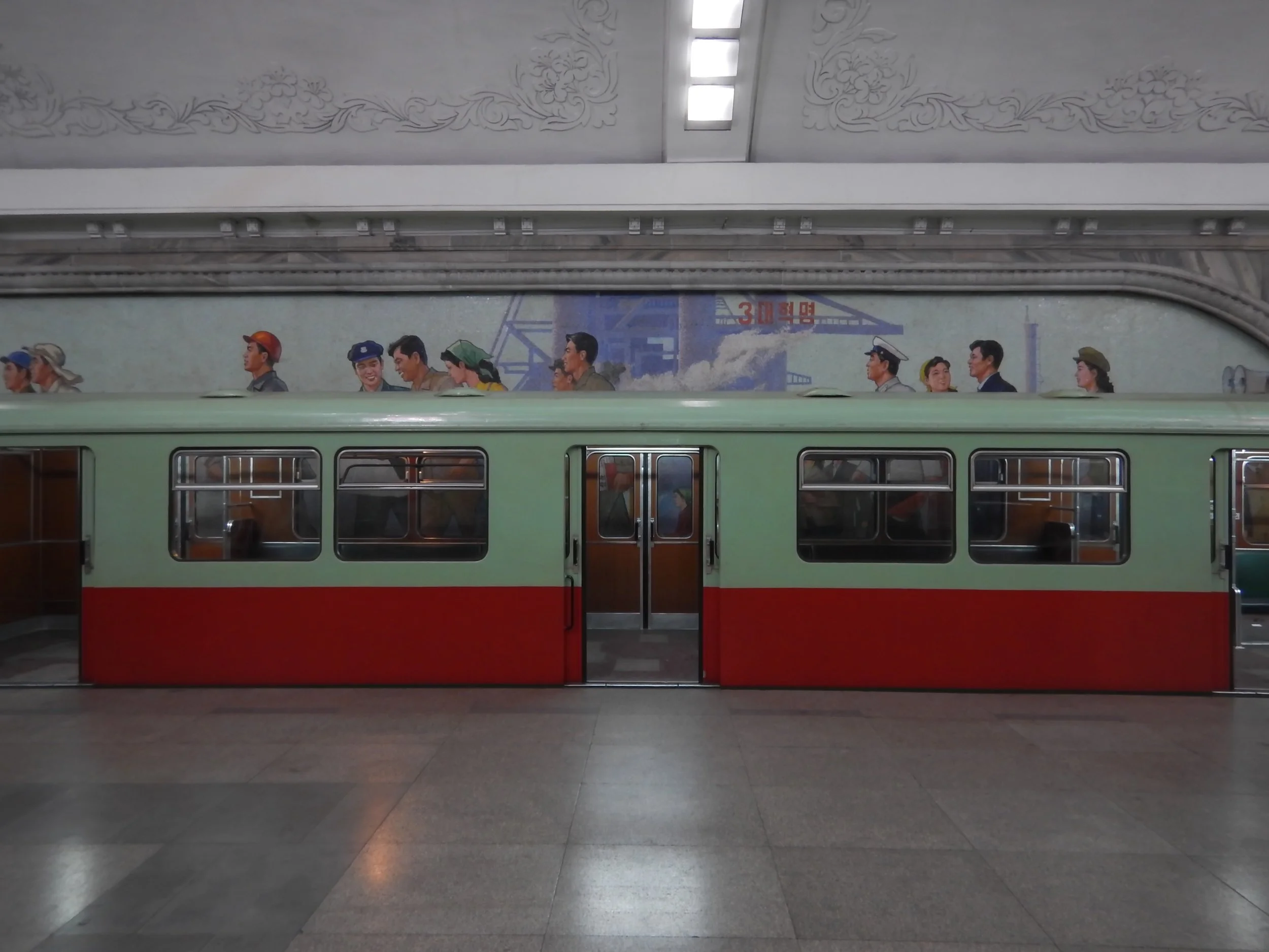 An empty subway car parked in the Pyongyang Metro's Puhung Station, found in the southern part of the city. Visible behind the car is a tile mosaic depicting the life of average North Korean workers. (Photo by Ethan Jakob Craft.)