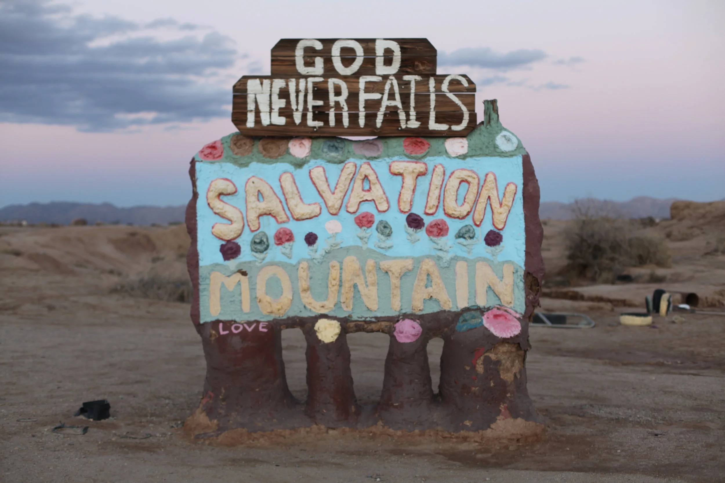 A crude sign welcomes visitors to Salvation Mountain in Slab City, Calif. at sunset on Jan. 6, 2017. (Photo by Ethan Jakob Craft.)