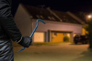 Picture of a burglar with a crowbar stalking a house