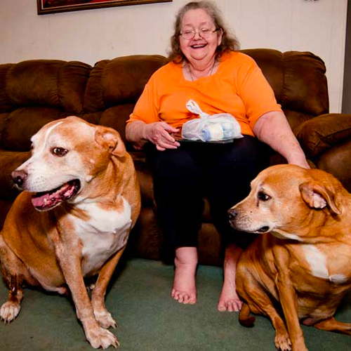 An+older+woman+poses+on+her+couch+with+two+big+dogs.jpeg