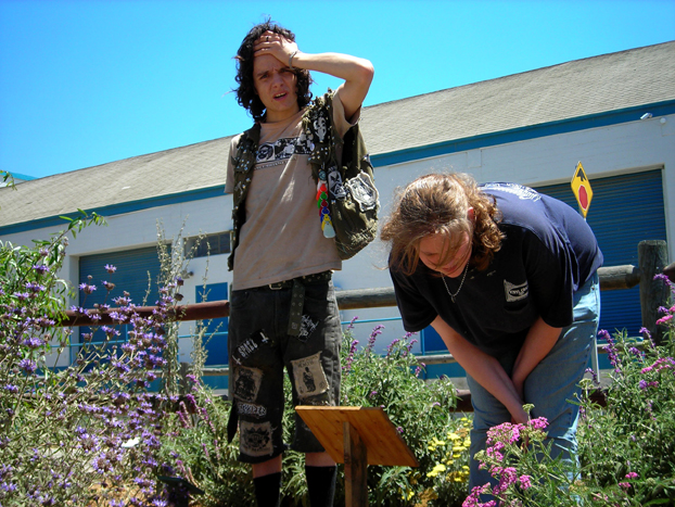 Daniel and Kyra reading new educational signage (purple Bee's Bliss in background, volunteer yellow evening primrose, and pink yarrow).