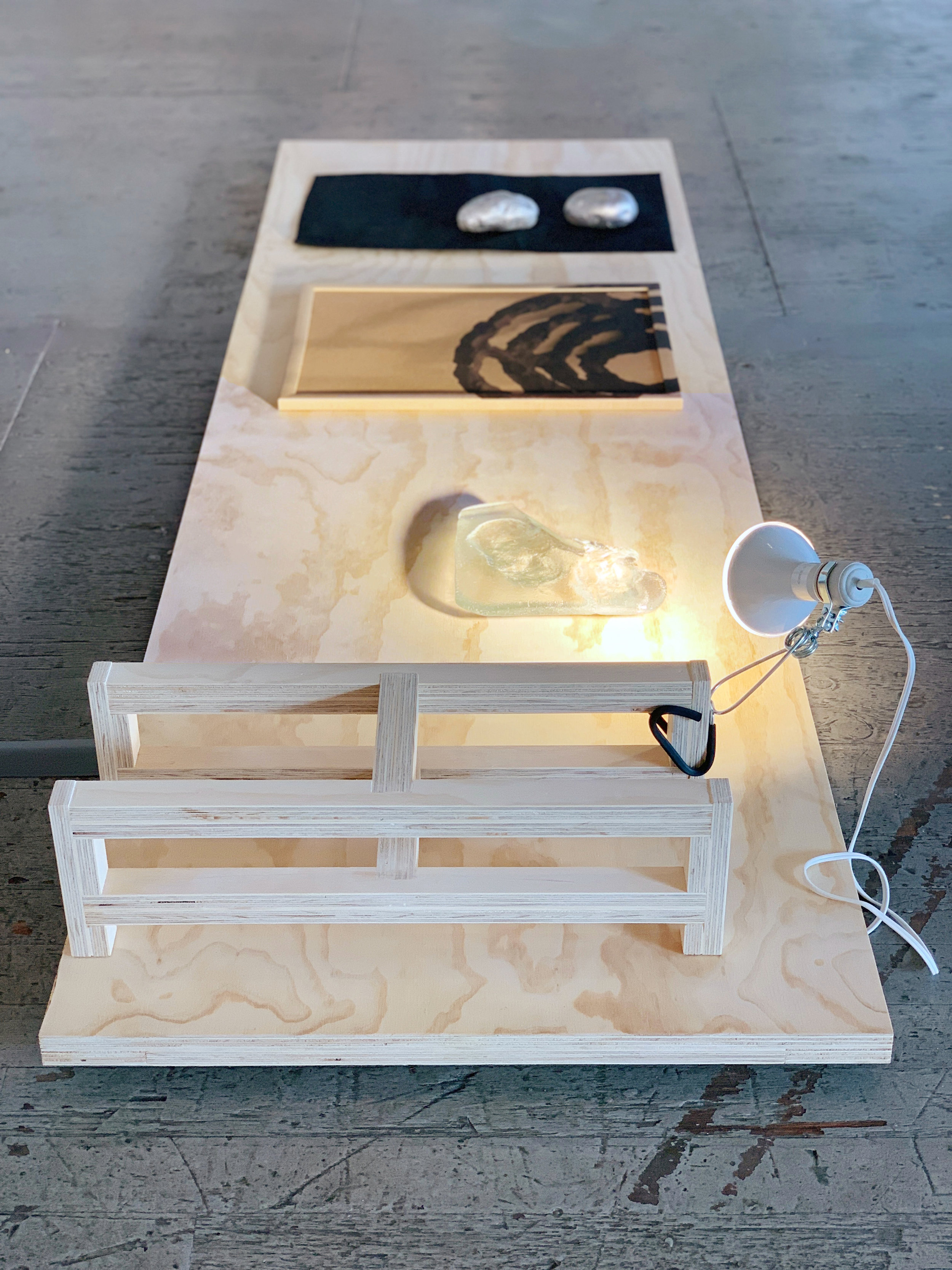   The Burrow , installation view, 2019, porcelain socket clamp light, LED bulb, plywood, sand-cast glass, acrylic on framed cork board, geotextile, cast aluminum, 21 x 38 x 96 inches 