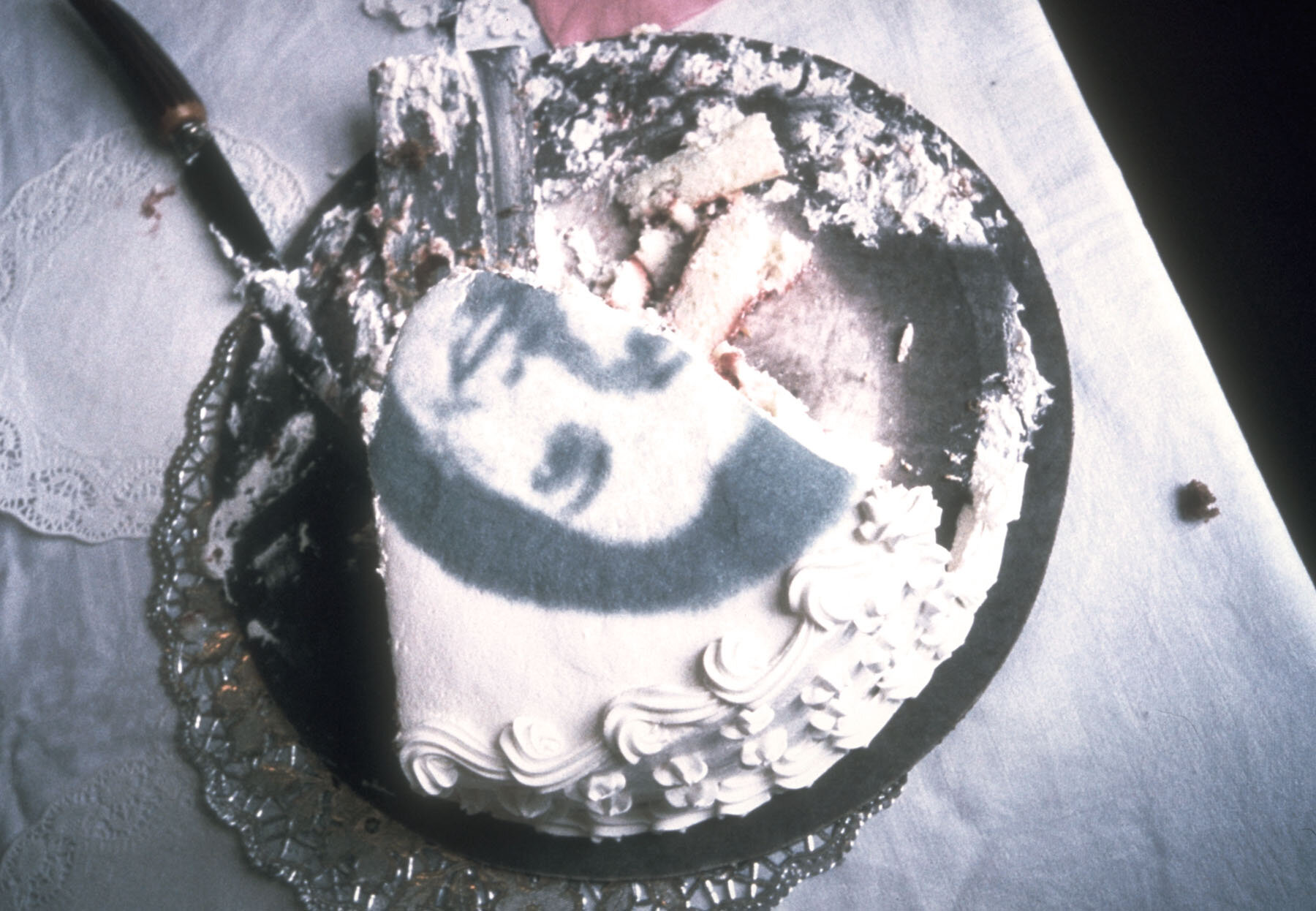   75 Ingredients , detail from performance, 1996, black food coloring on 12-inch edible round cake, silver cake board, doilies, knife 