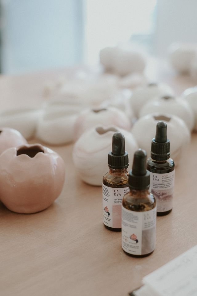 Three La-Eva essential oil dropper bottles among handmade pink and white ceramic inhalation pomegranates on a timber table at Casa Fuzetta in Olhão.